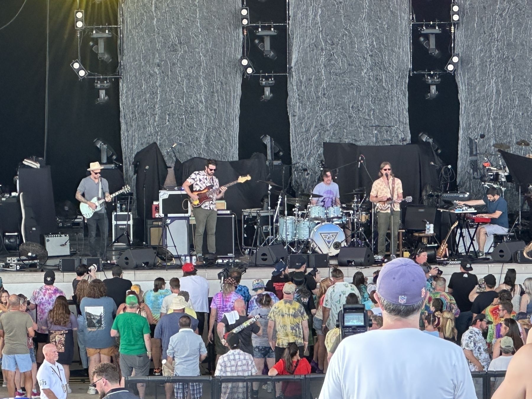 A band is performing on stage in front of a crowd at an outdoor concert.