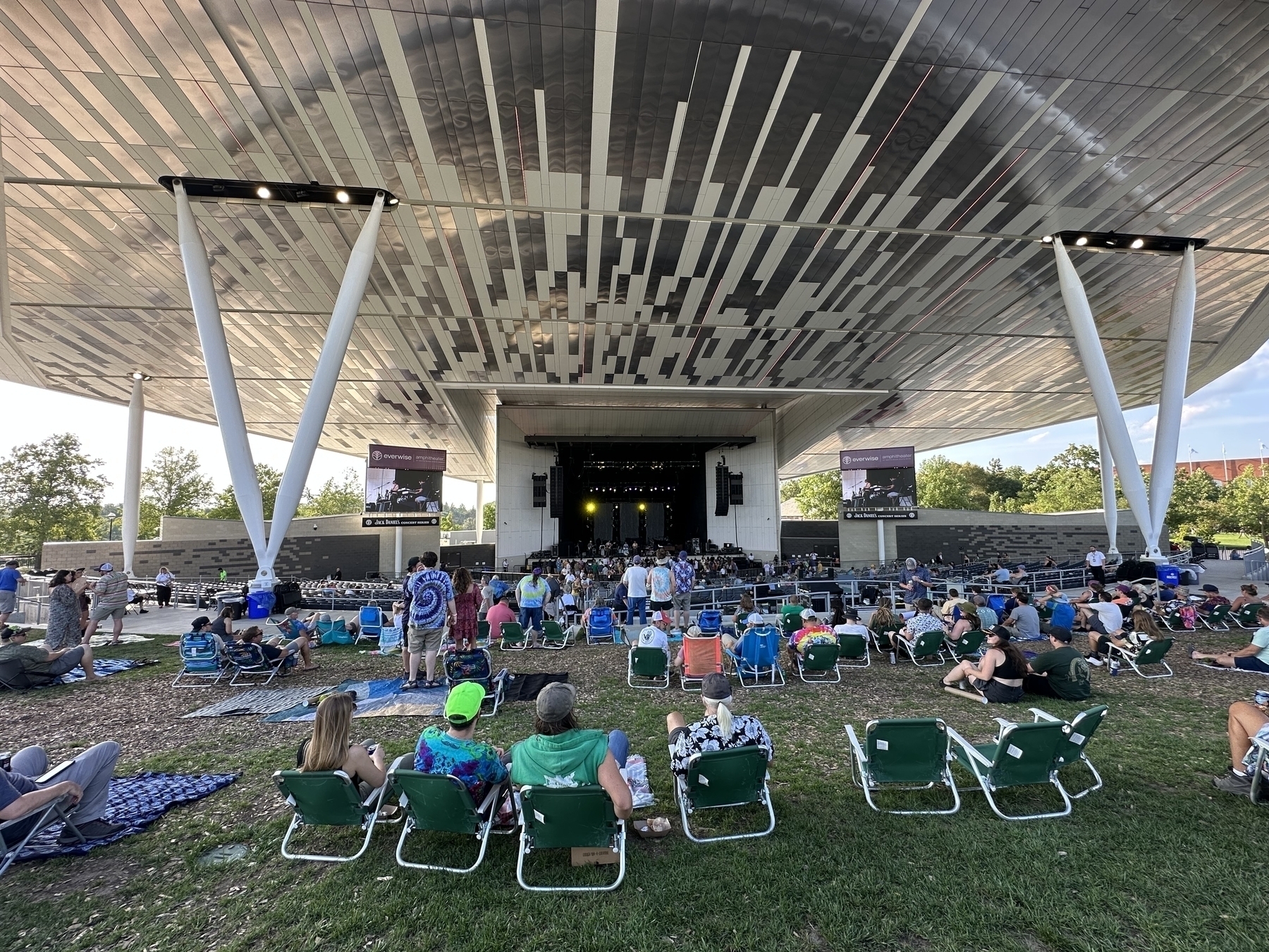 People are seated on chairs and the ground, watching a performance on an outdoor stage.