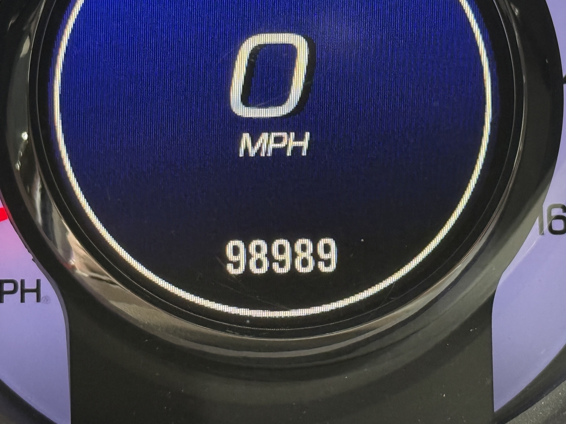 A car's digital speedometer displays 0 MPH, with an odometer reading of 98,989.