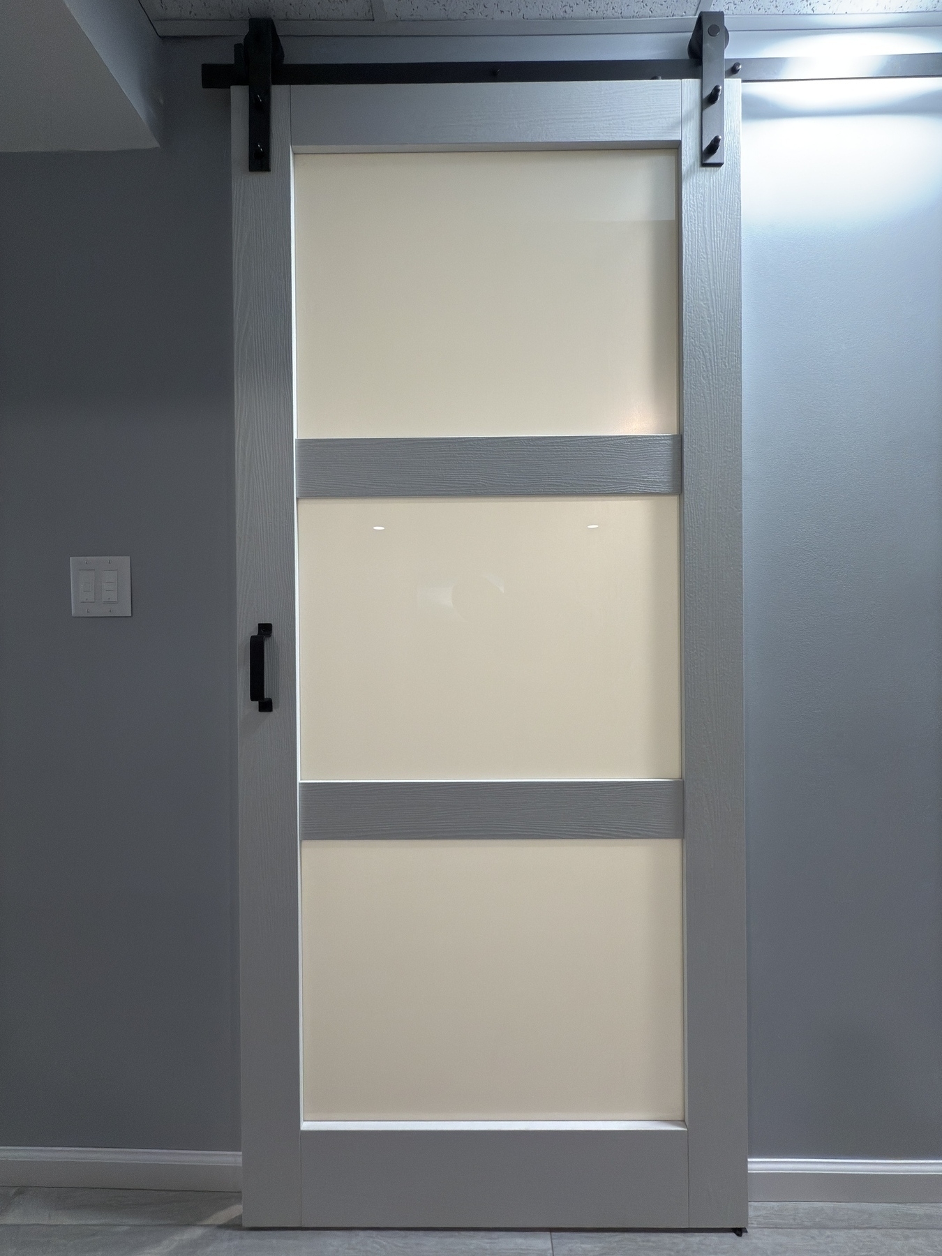 A modern, frosted glass barn door with a sleek handle is mounted on a sliding track against a gray wall.