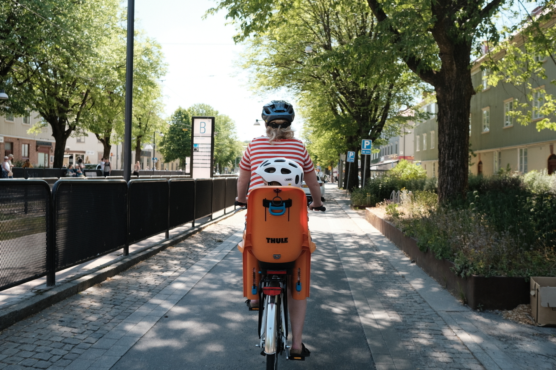 Foto av kvinna och barn på cykel, cyklandes på en cykelbana i stan. 
