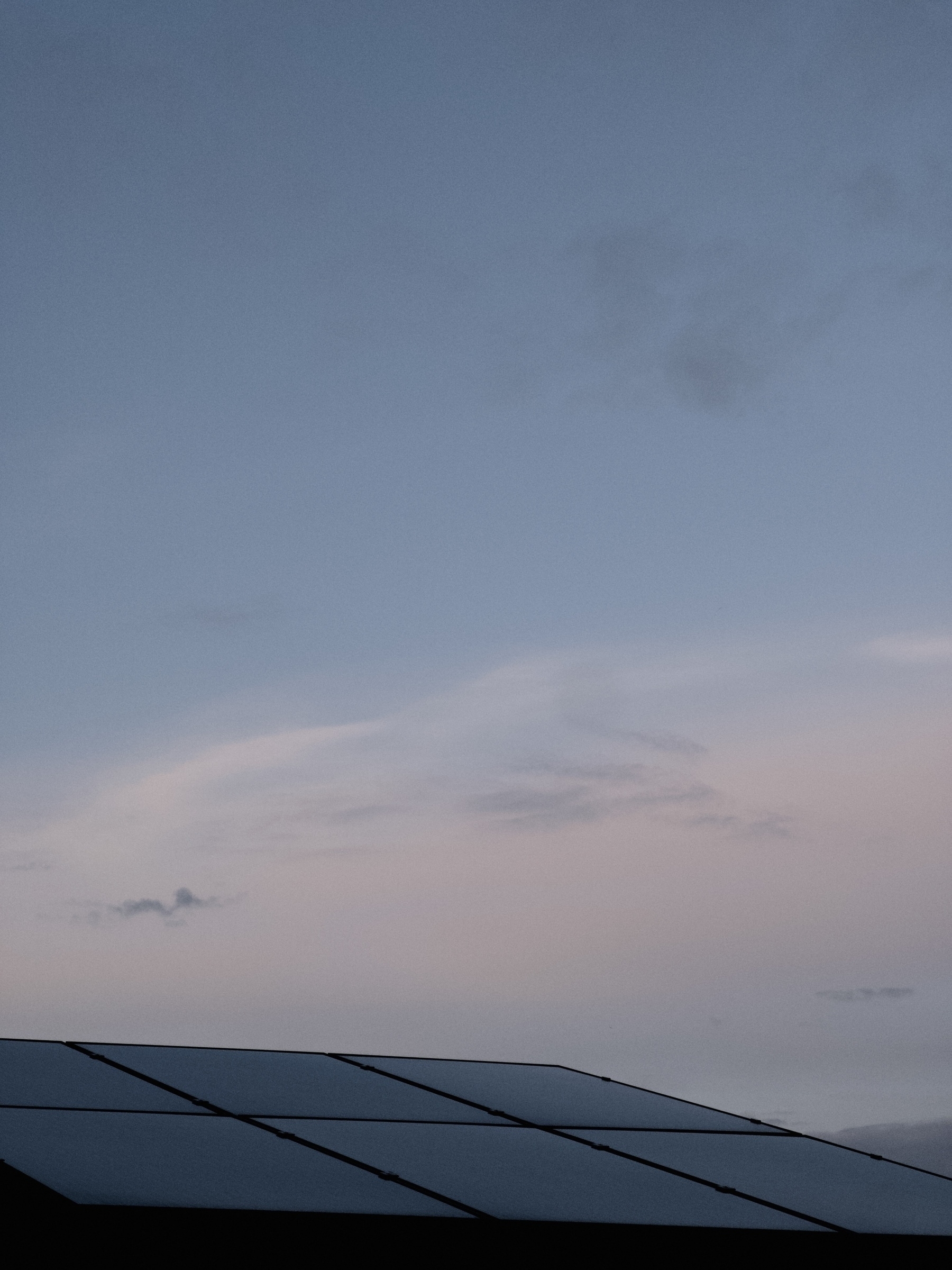 Foto av ett hustak med solpaneler. I bakgrunden är det en disig blå himmel. 