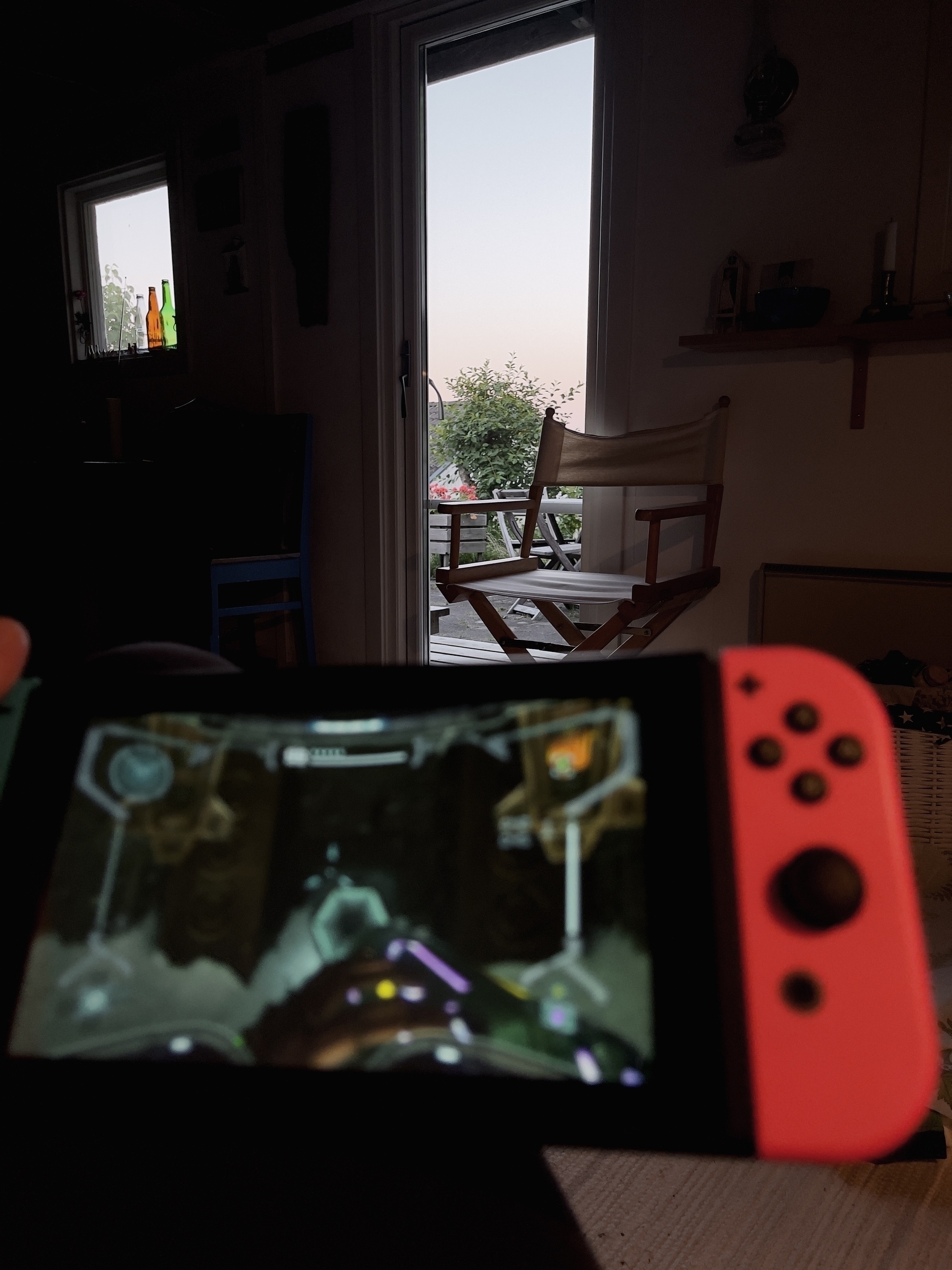 A person is playing a video game on a handheld console with a view of a porch and outdoor scenery in the background.