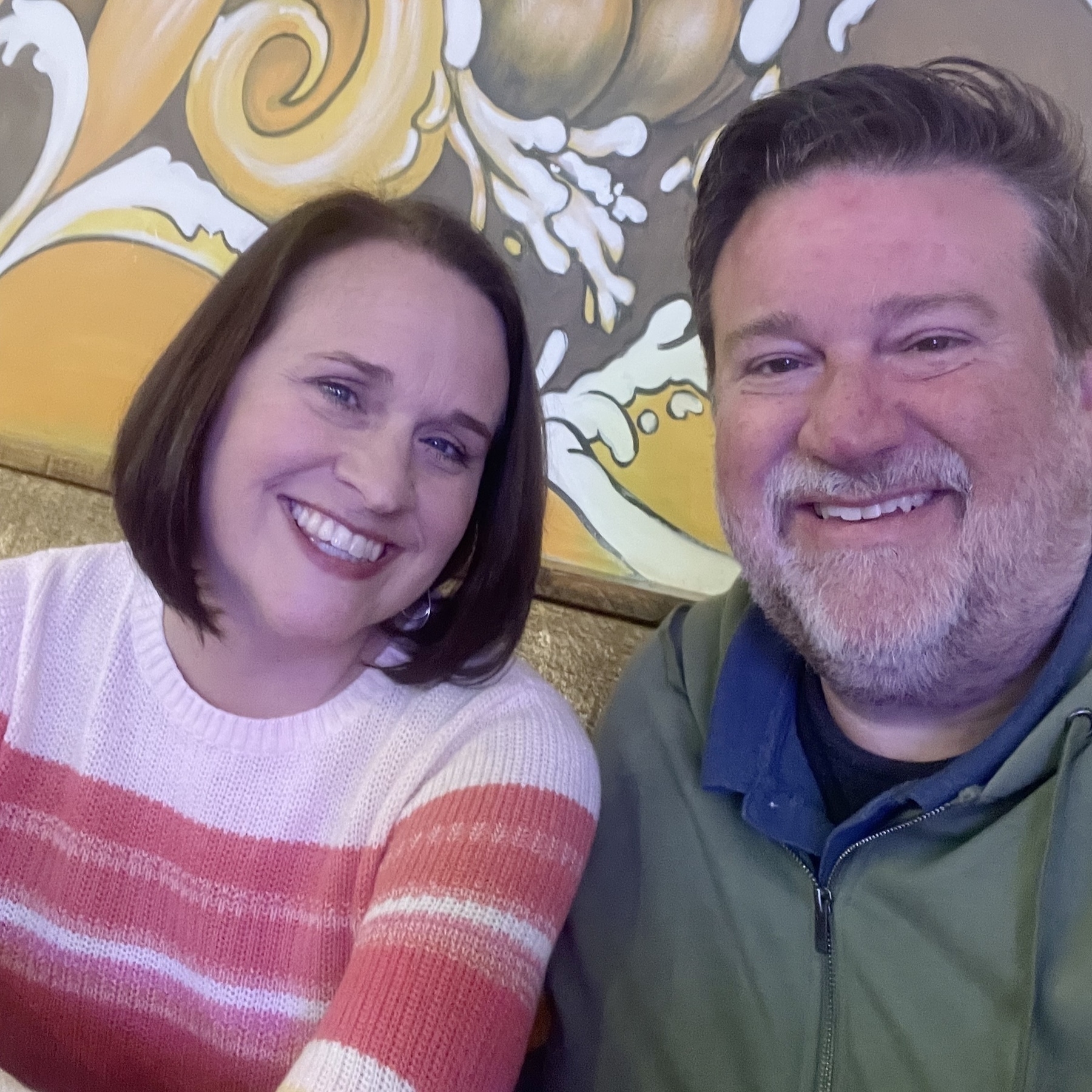 Bob and Liz are sitting together in front of a colorful wall mural.