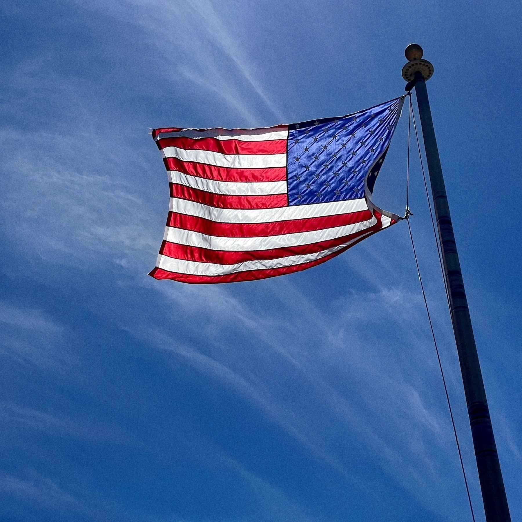 American flag on a flag pole blowing in the wind with a blue sky.