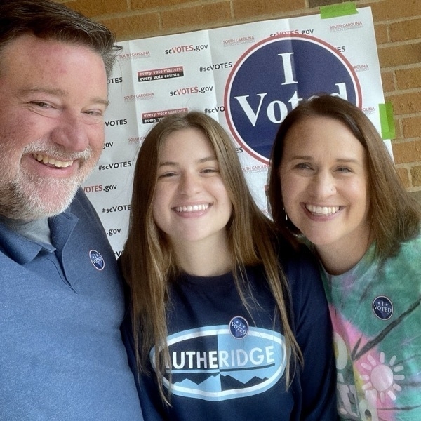 Three people smiling in front of an 'I voted' sign.