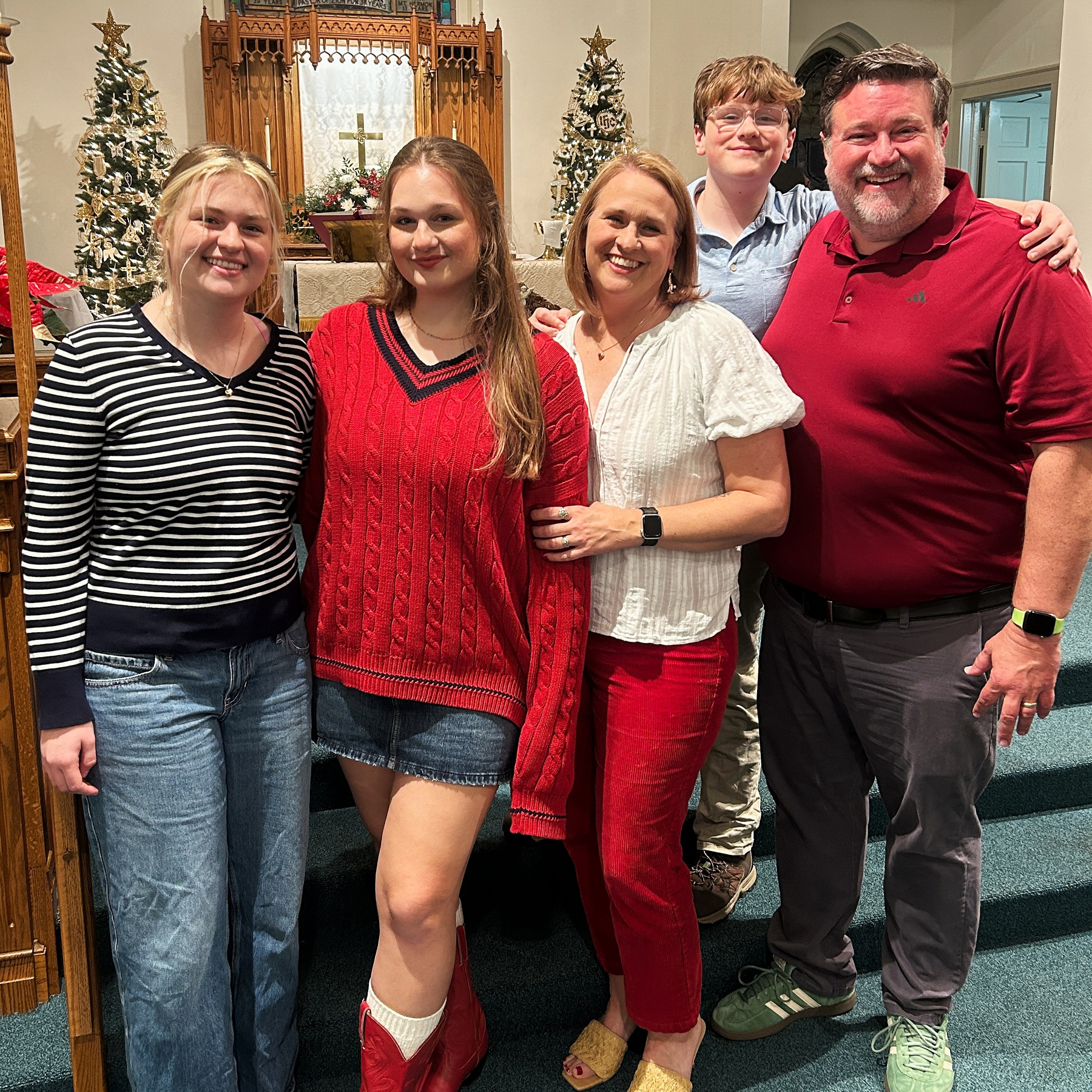 A family of five poses together dressed in festive attire, with Christmas trees and decorations in the background.