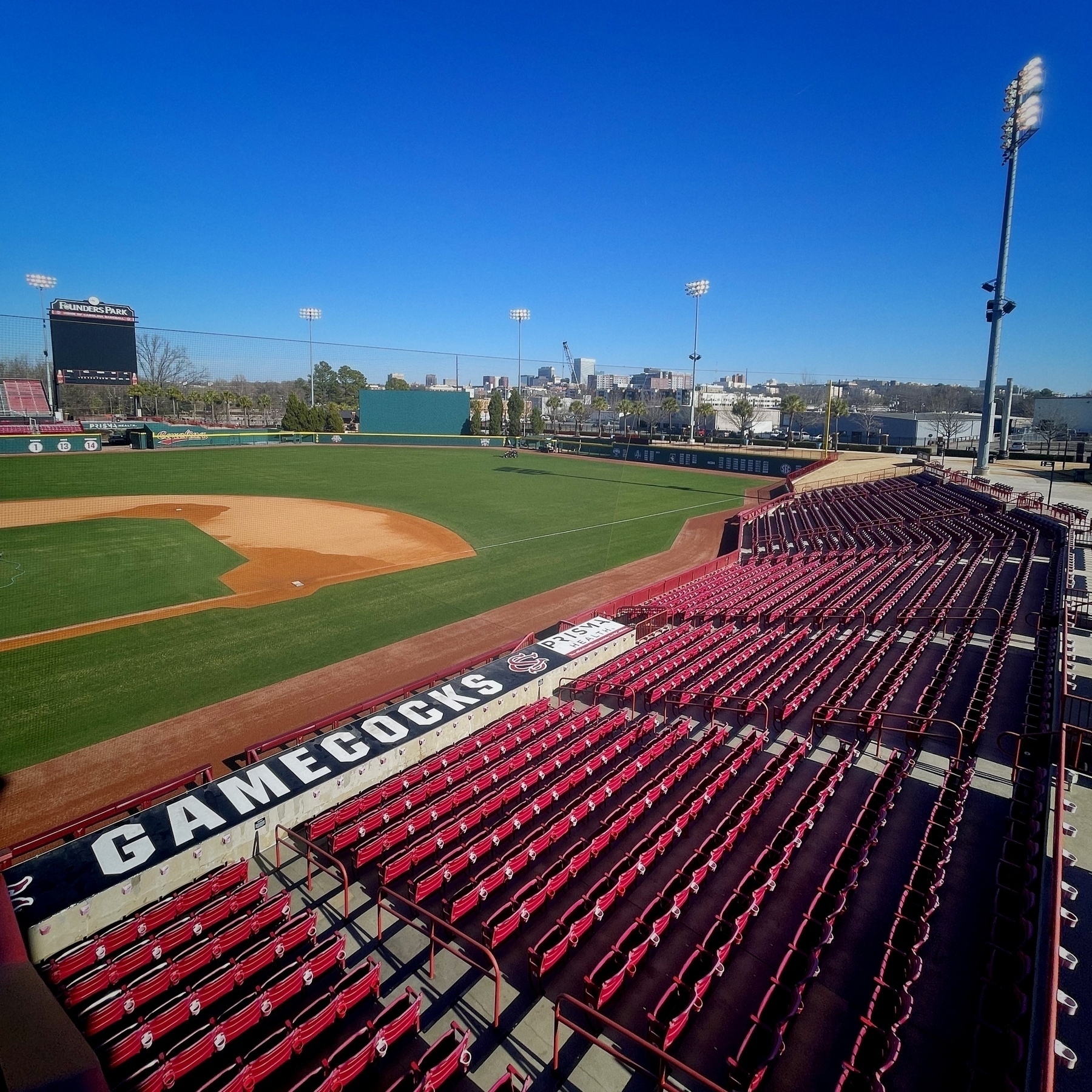 The University of South Carolina baseball stadium with garnet seats, featuring an empty field and a city skyline in the background.