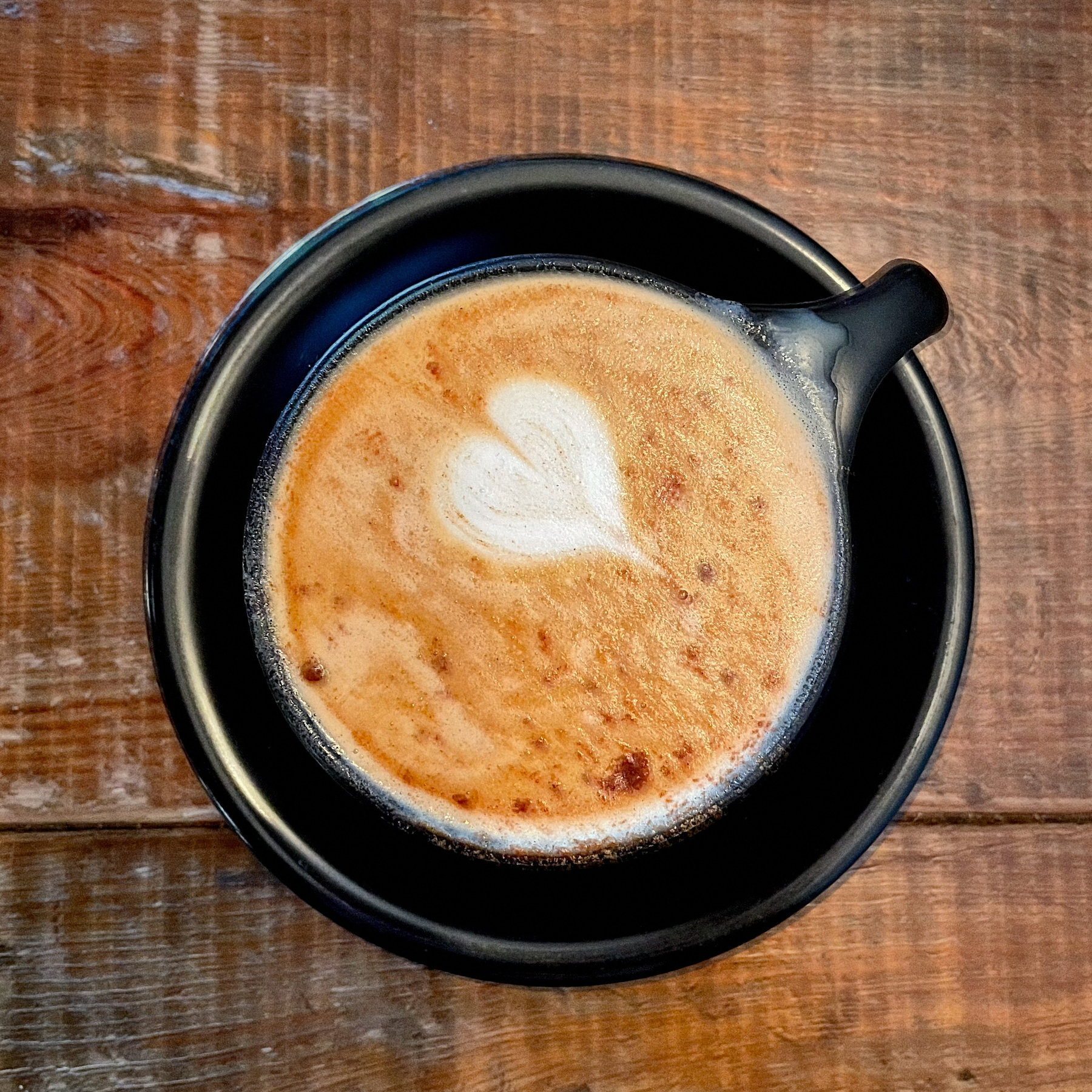 A cubano with a heart-shaped latte art on a wooden table.
