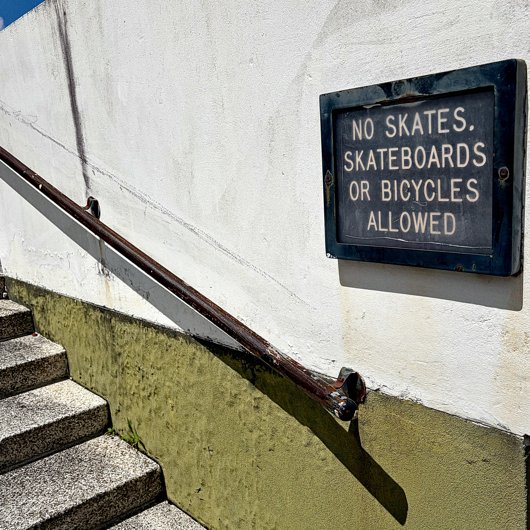 A sign on a wall by a staircase states NO SKATES, SKATEBOARDS OR BICYCLES ALLOWED.