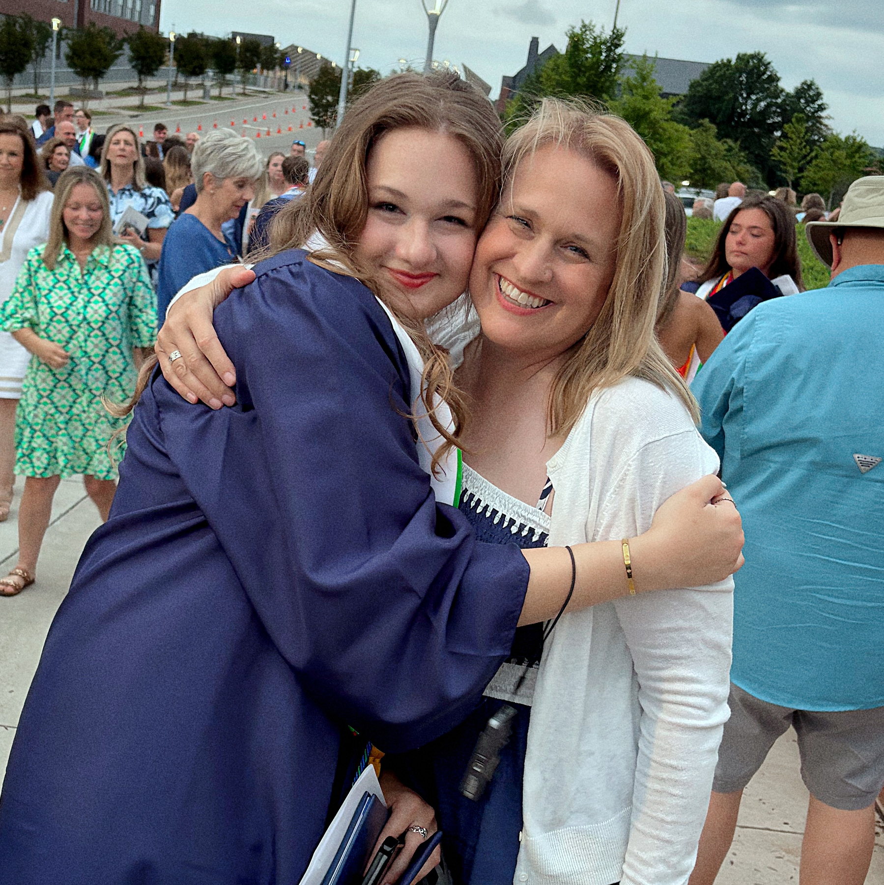 Two people are happily embracing at an outdoor event, with other attendees in the background.