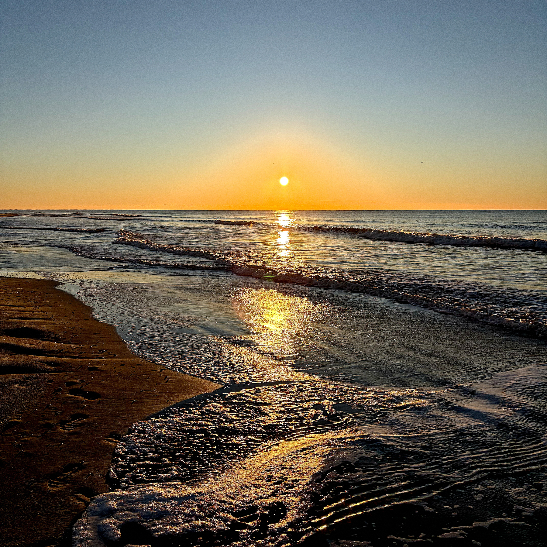 A serene beach scene at sunrise, with gentle waves lapping the shore.