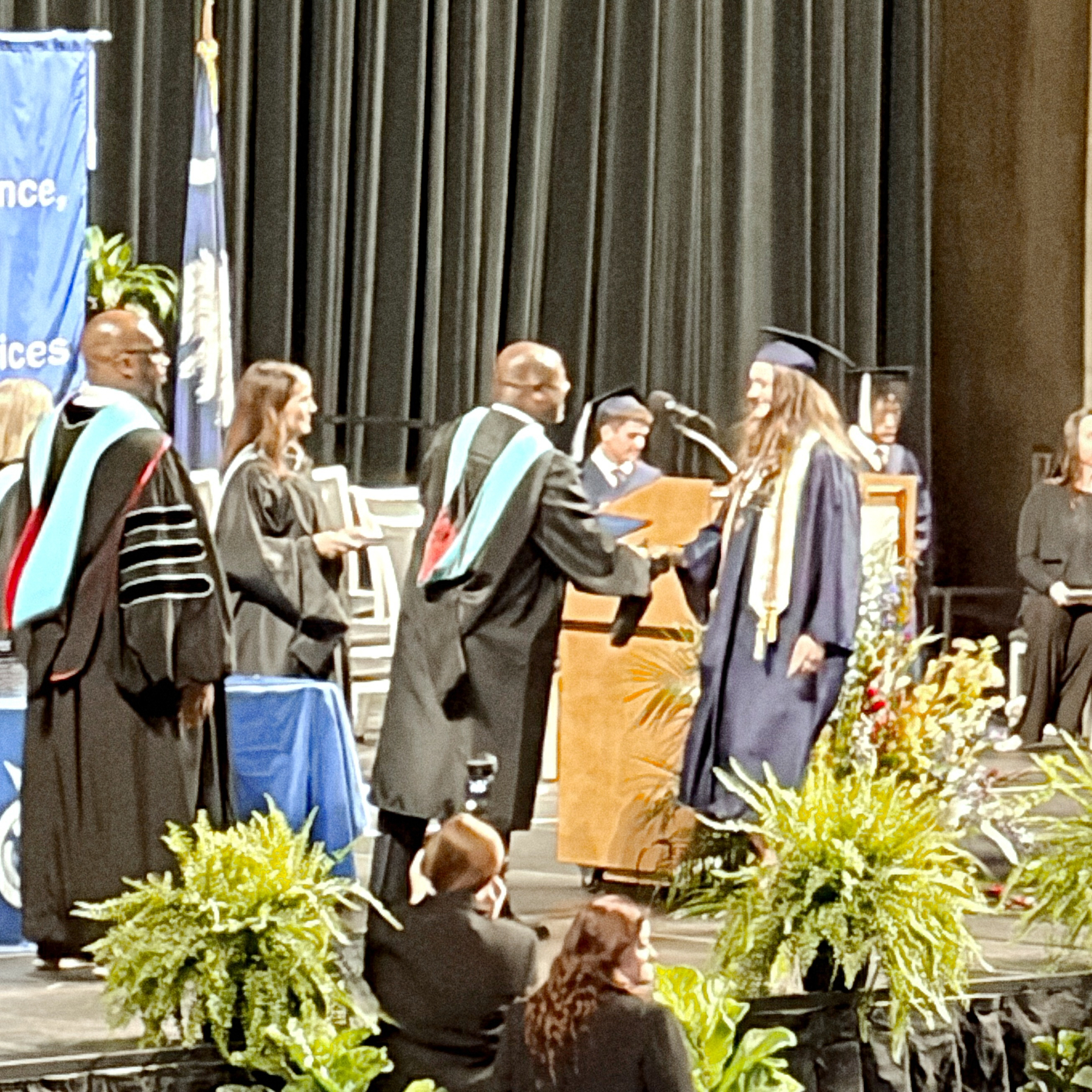 A graduate in a cap and gown is receiving their diploma on stage during a graduation ceremony.
