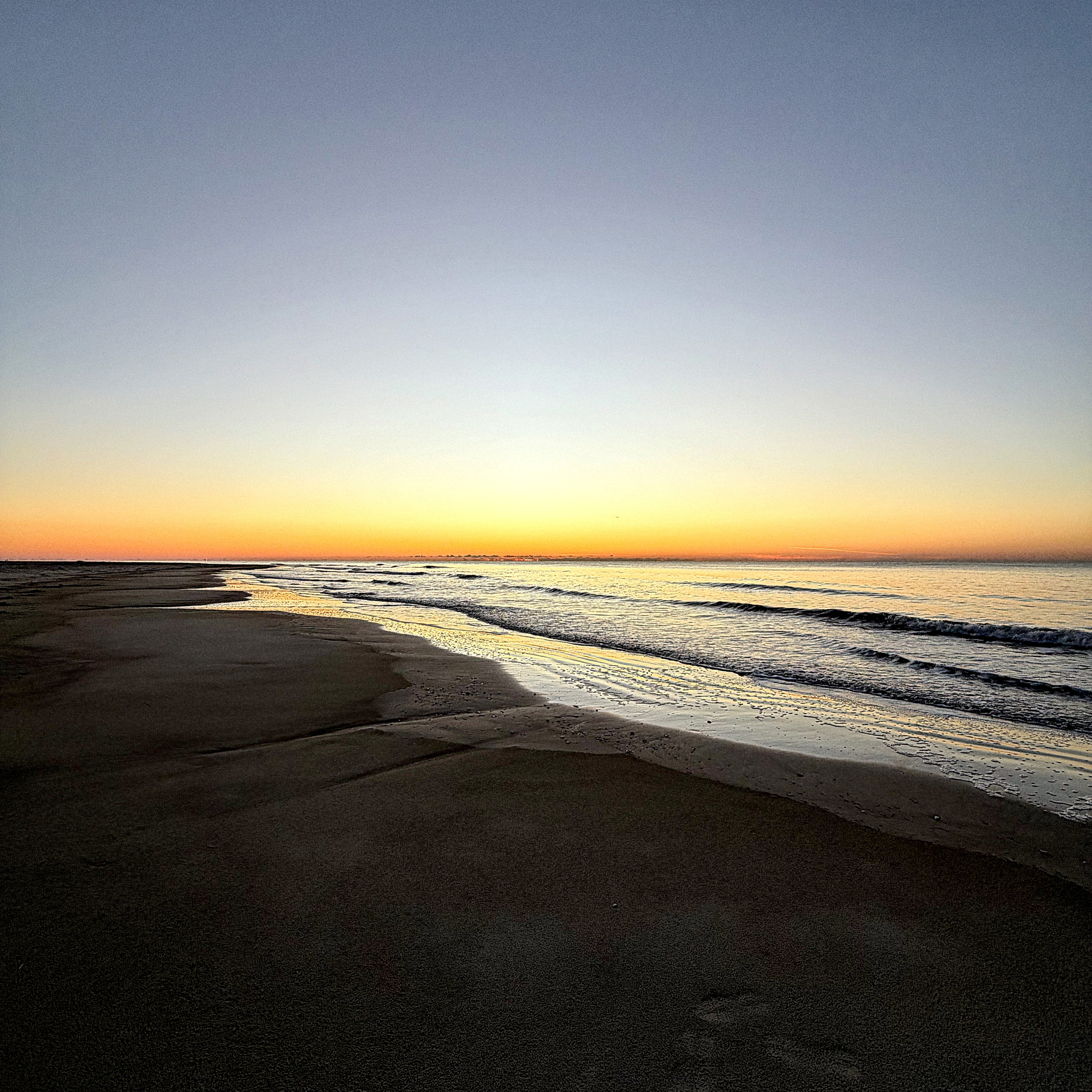 A serene beach scene features a calm shoreline with gentle waves under a colorful sunrise sky.