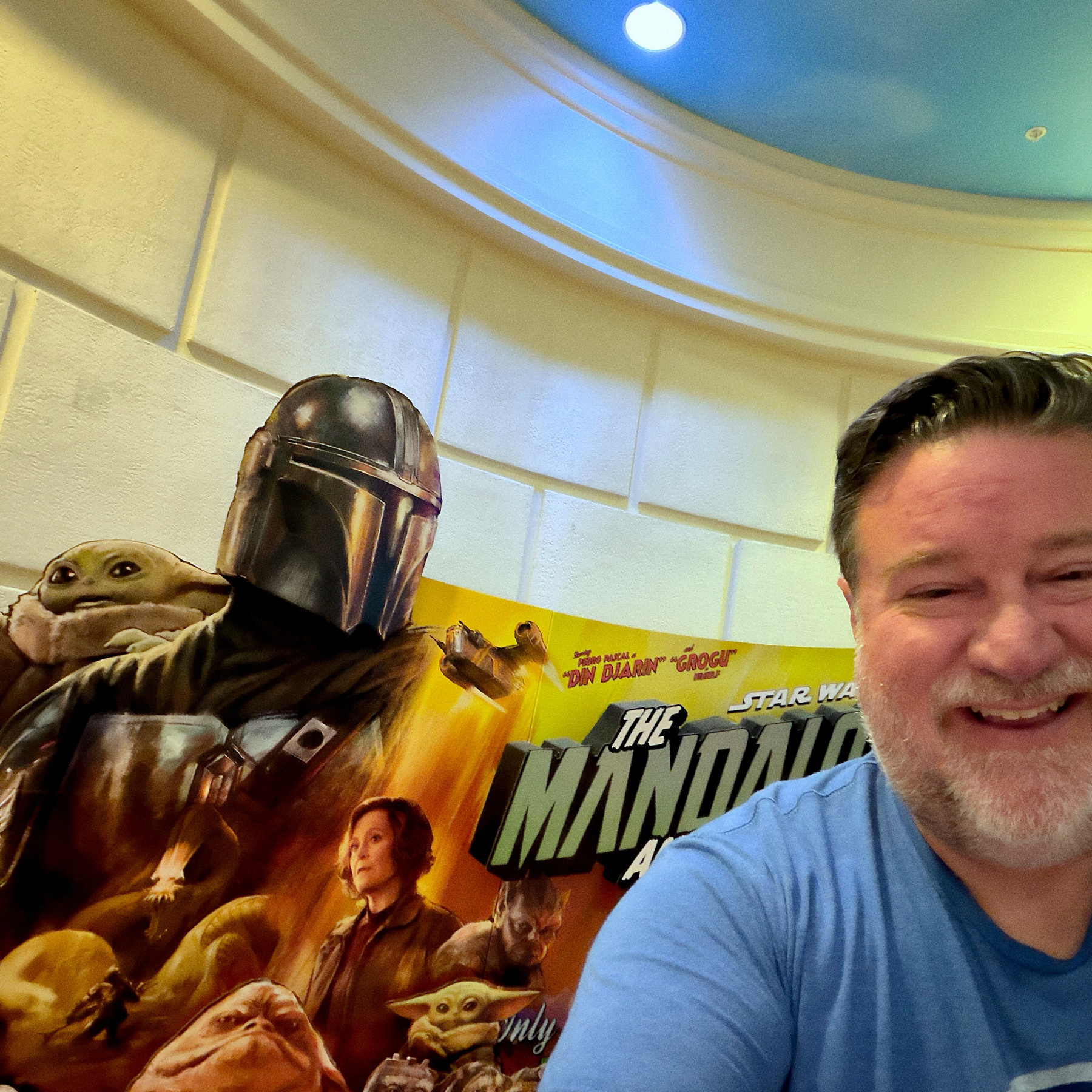 A person is smiling next to a display featuring characters from The Mandalorian.