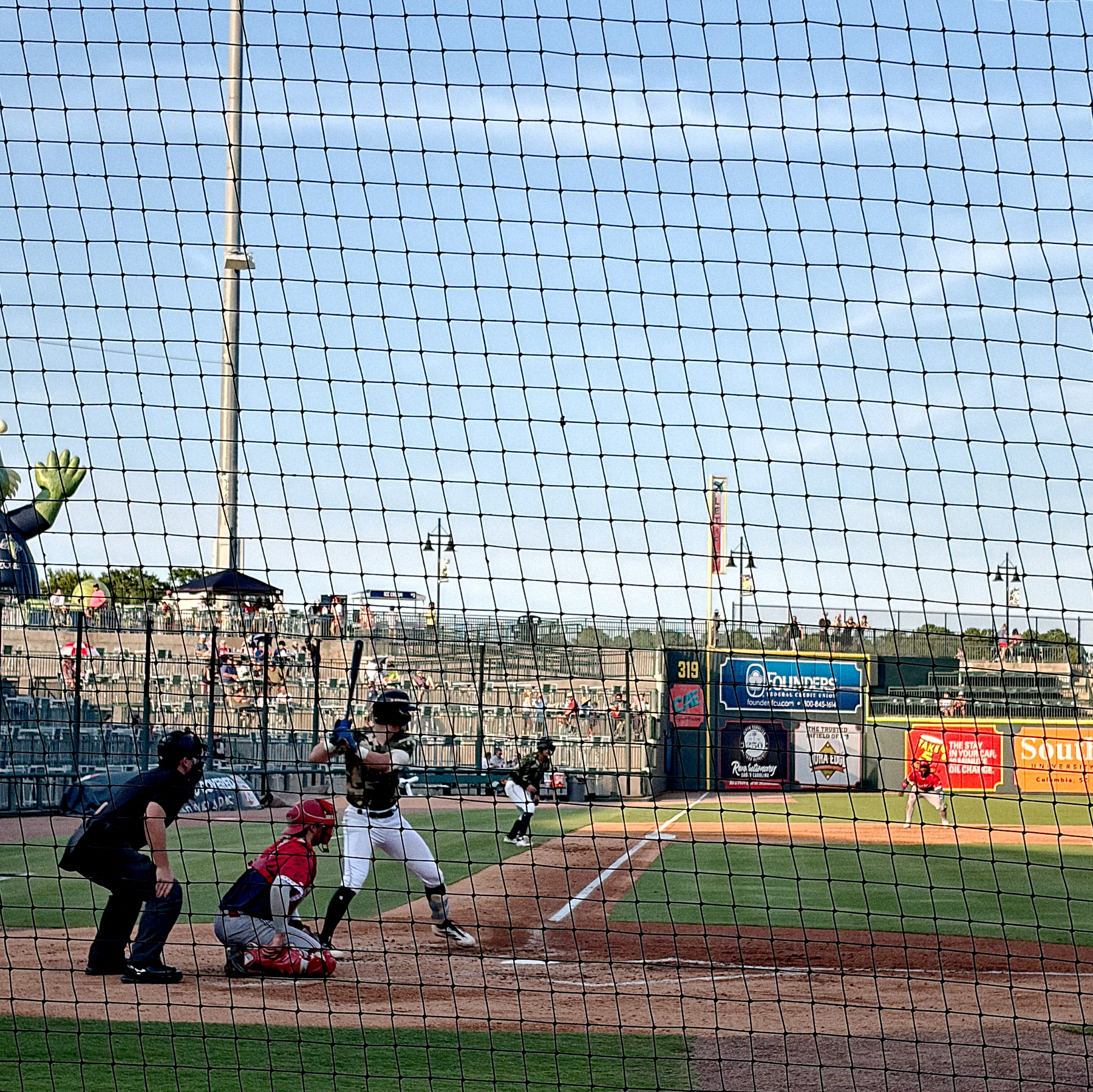 A baseball player is at bat while the catcher, umpire, and other players are positioned on the field during a game.