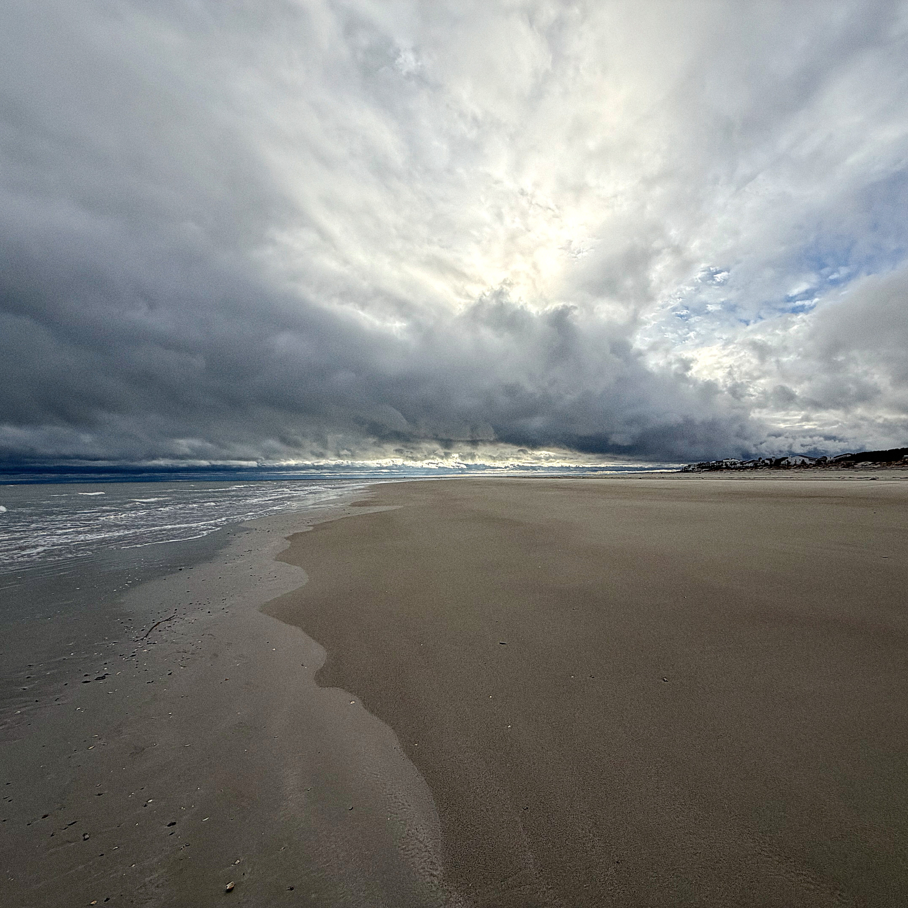 A vast, empty beach stretches towards the horizon under a dramatic, cloud-filled sky.