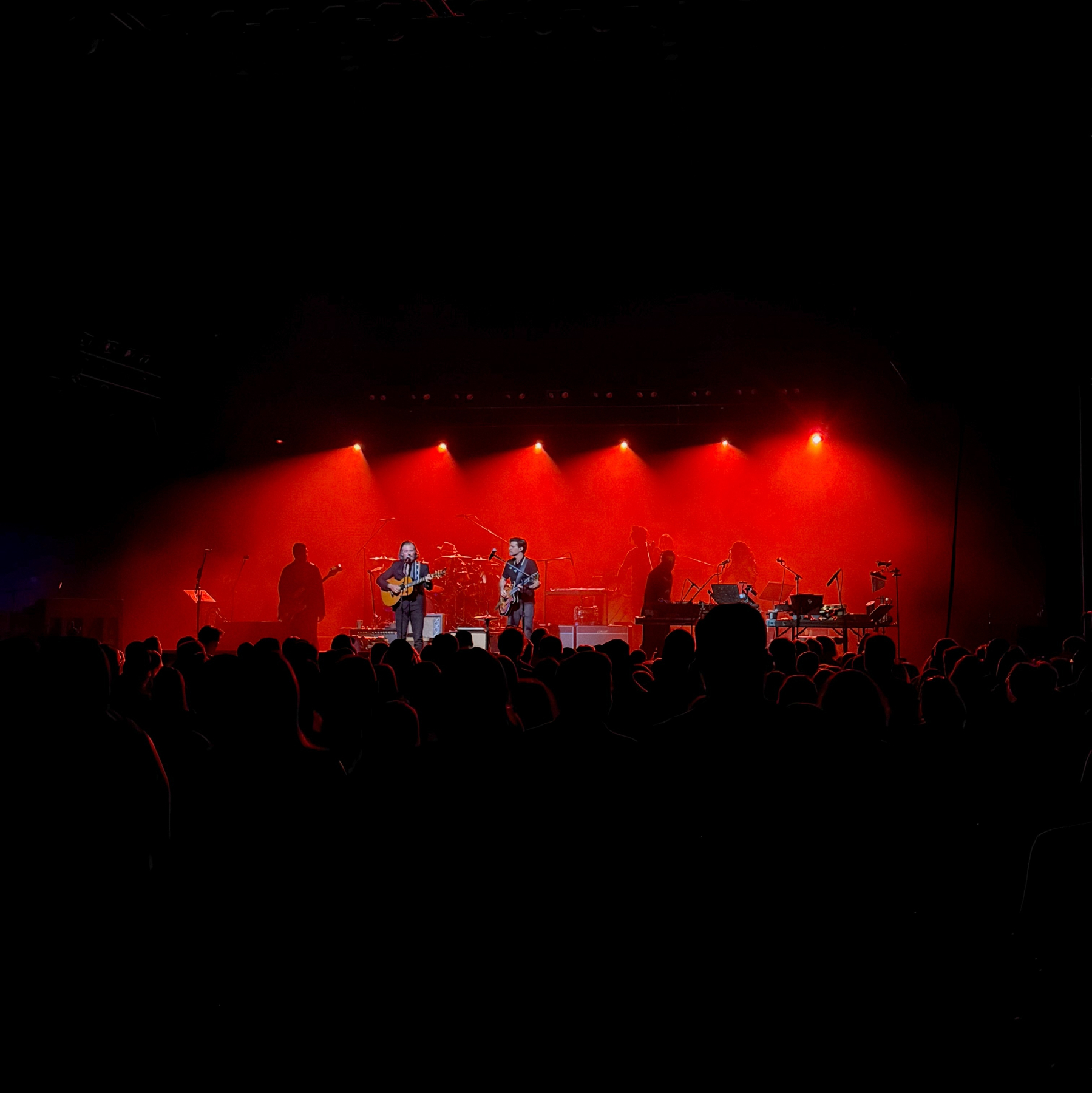 The Avett Brothers perform on stage under red lighting before an audience.