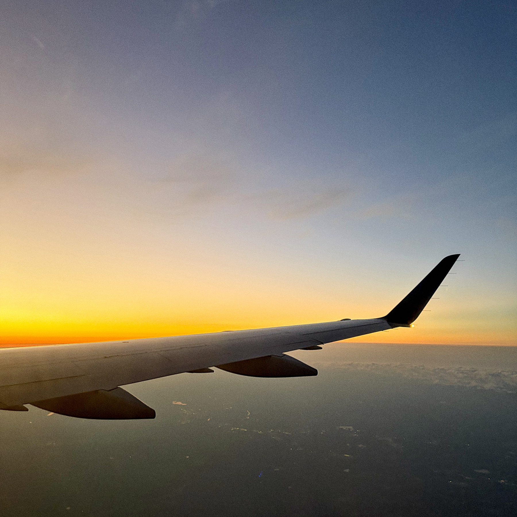 A view of an airplane wing flying above the clouds during a vibrant sunset.