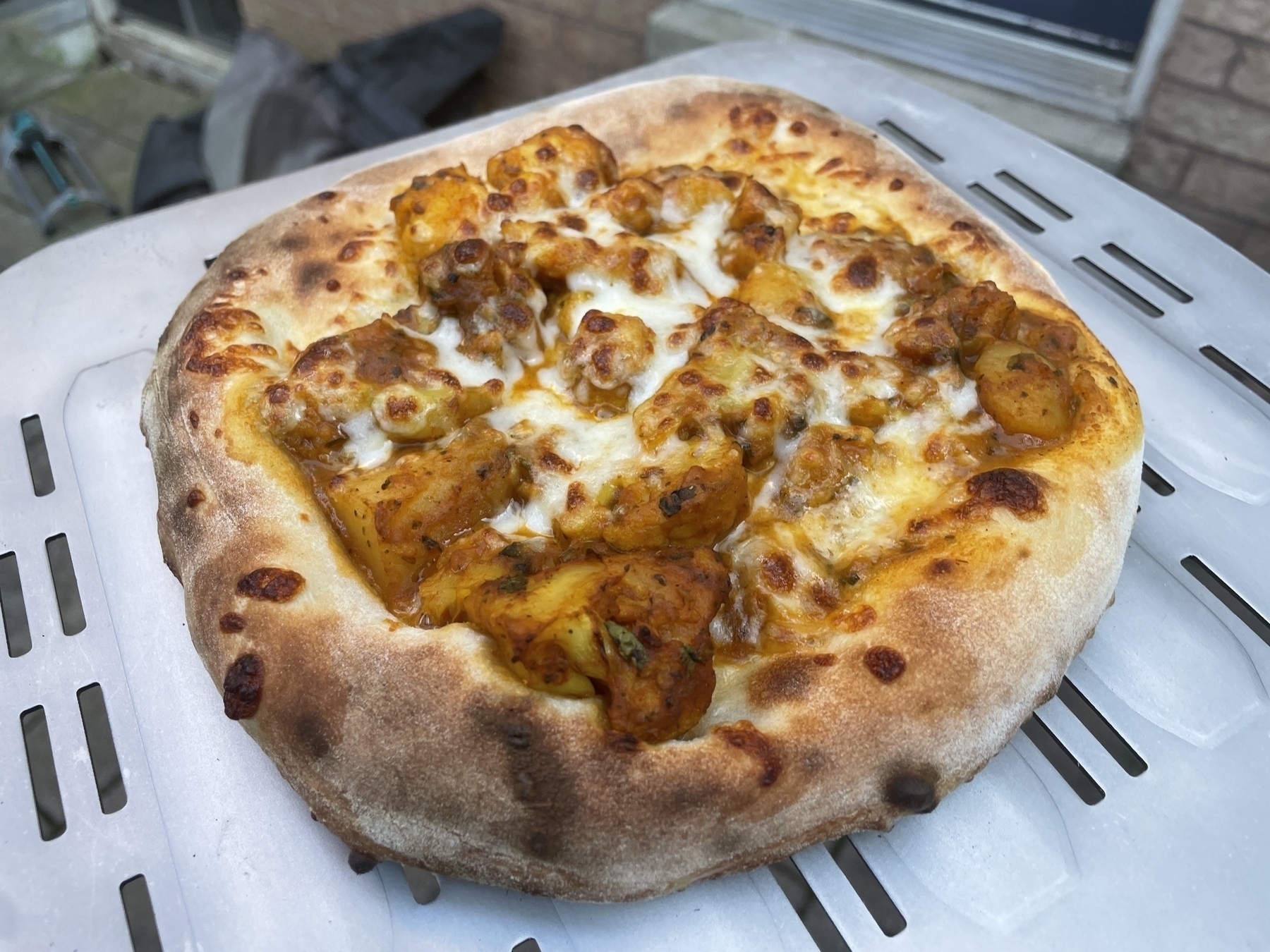 Pizza on a pizza peel with aloo gobi toppings.