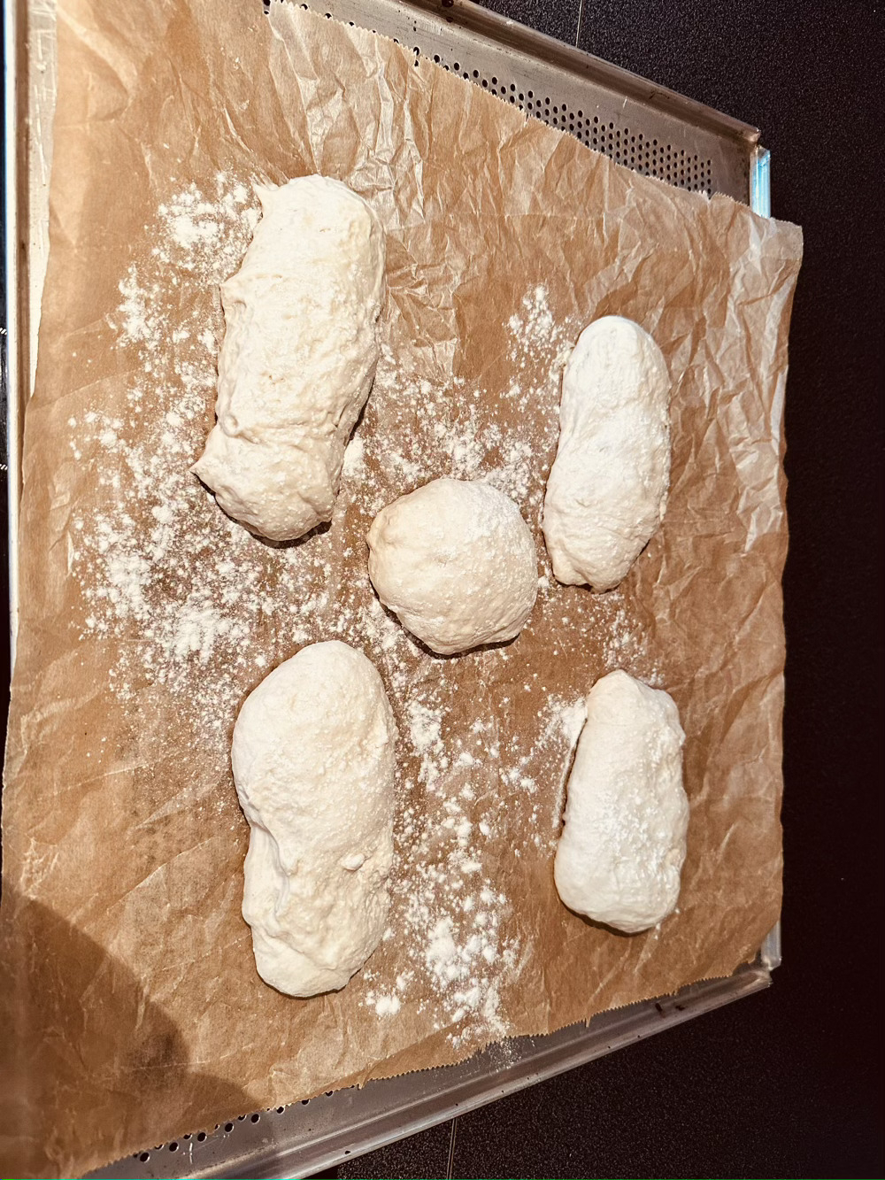 4 oblong and 1 round bread roll on baking parchment on a holed baking sheet