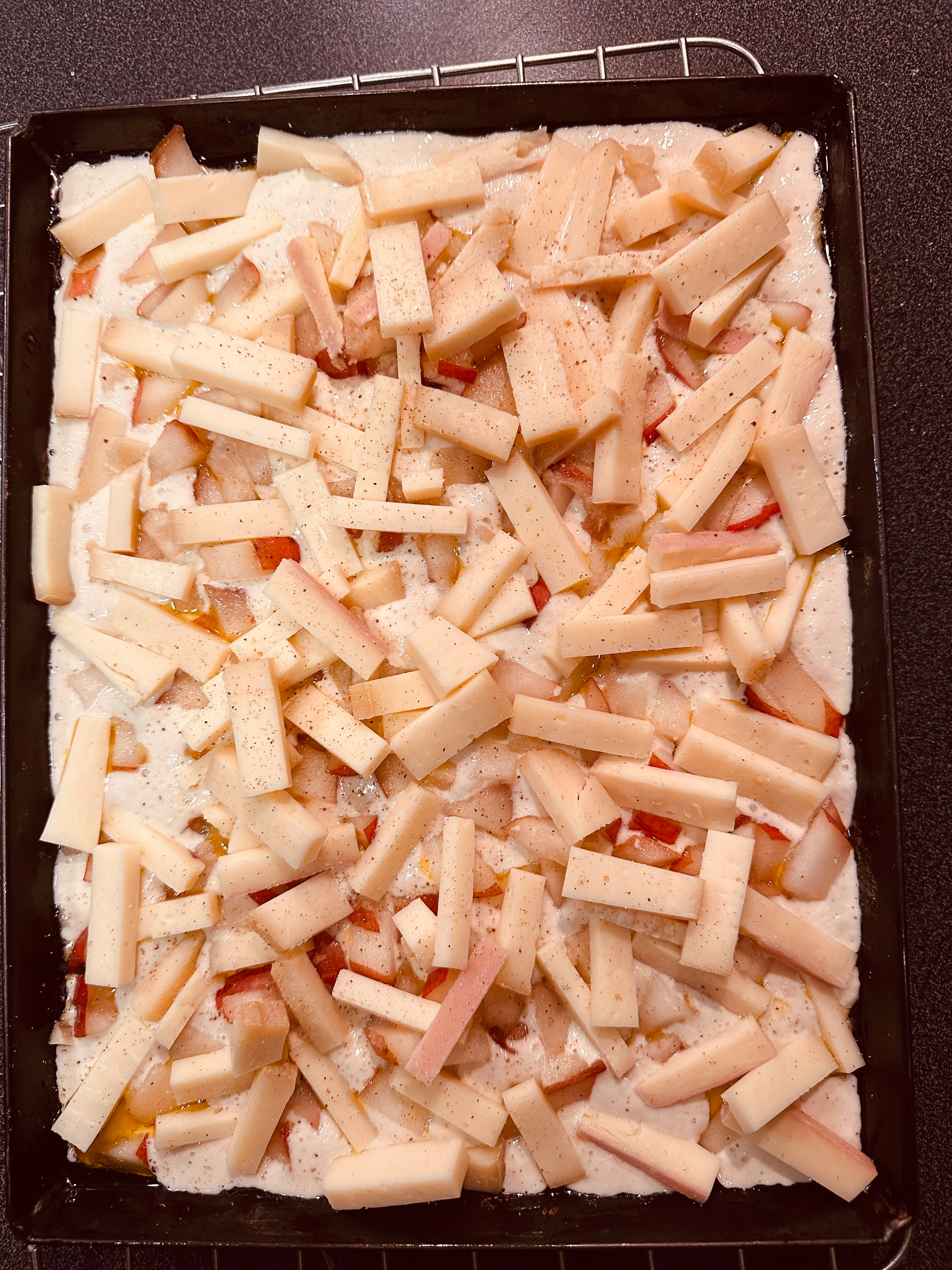 Sliced pear and raclette cheese are arranged on a focaccia dough in a baking tray.