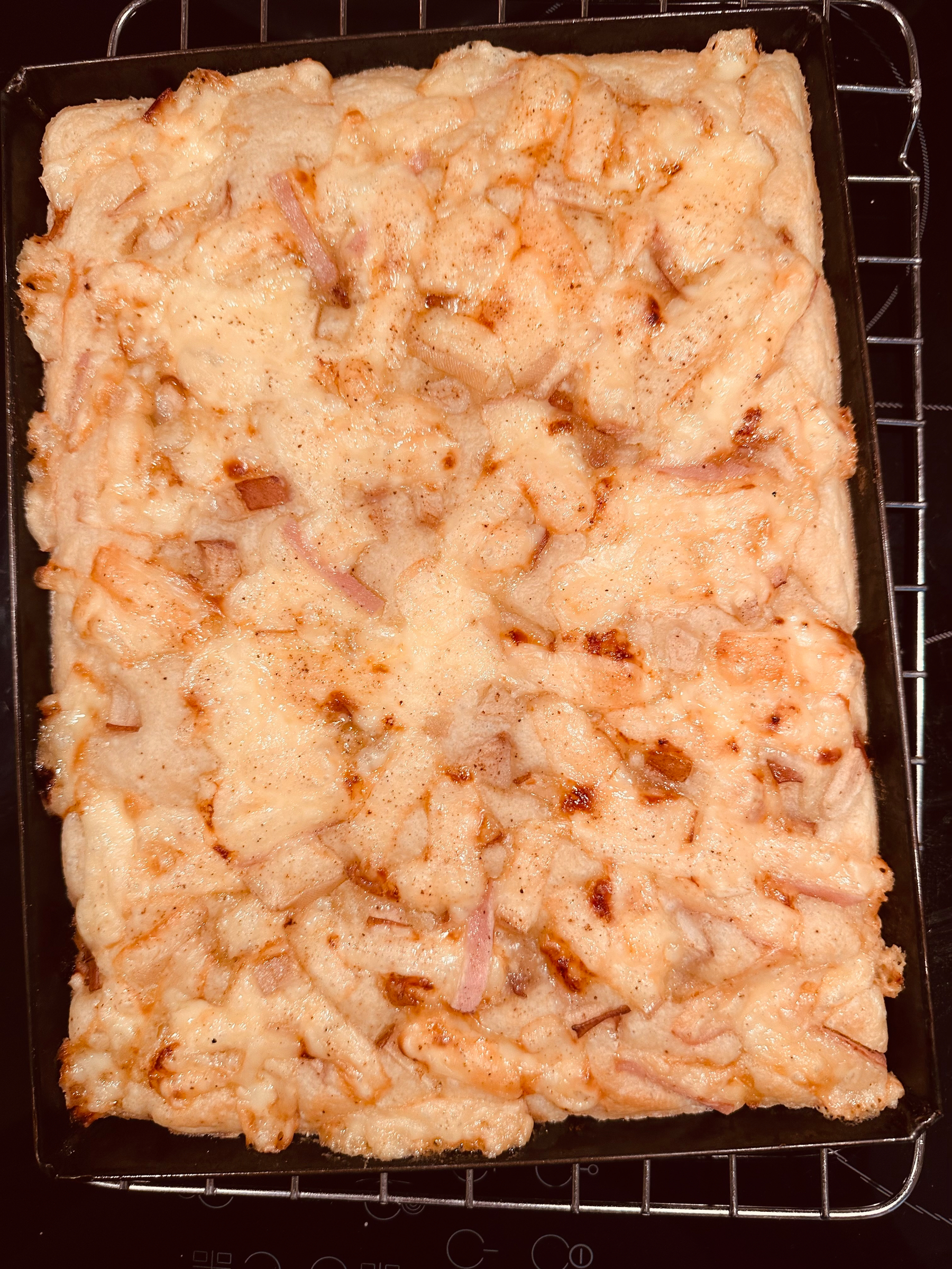 A rectangular focaccia topped with pear and melted cheese sits on a baking tray.