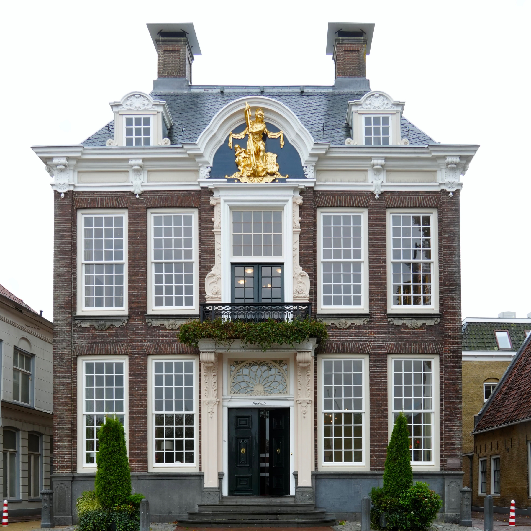 A large, ornate brick building with white trim, tall windows, and a golden statue adorning the top center of its facade.