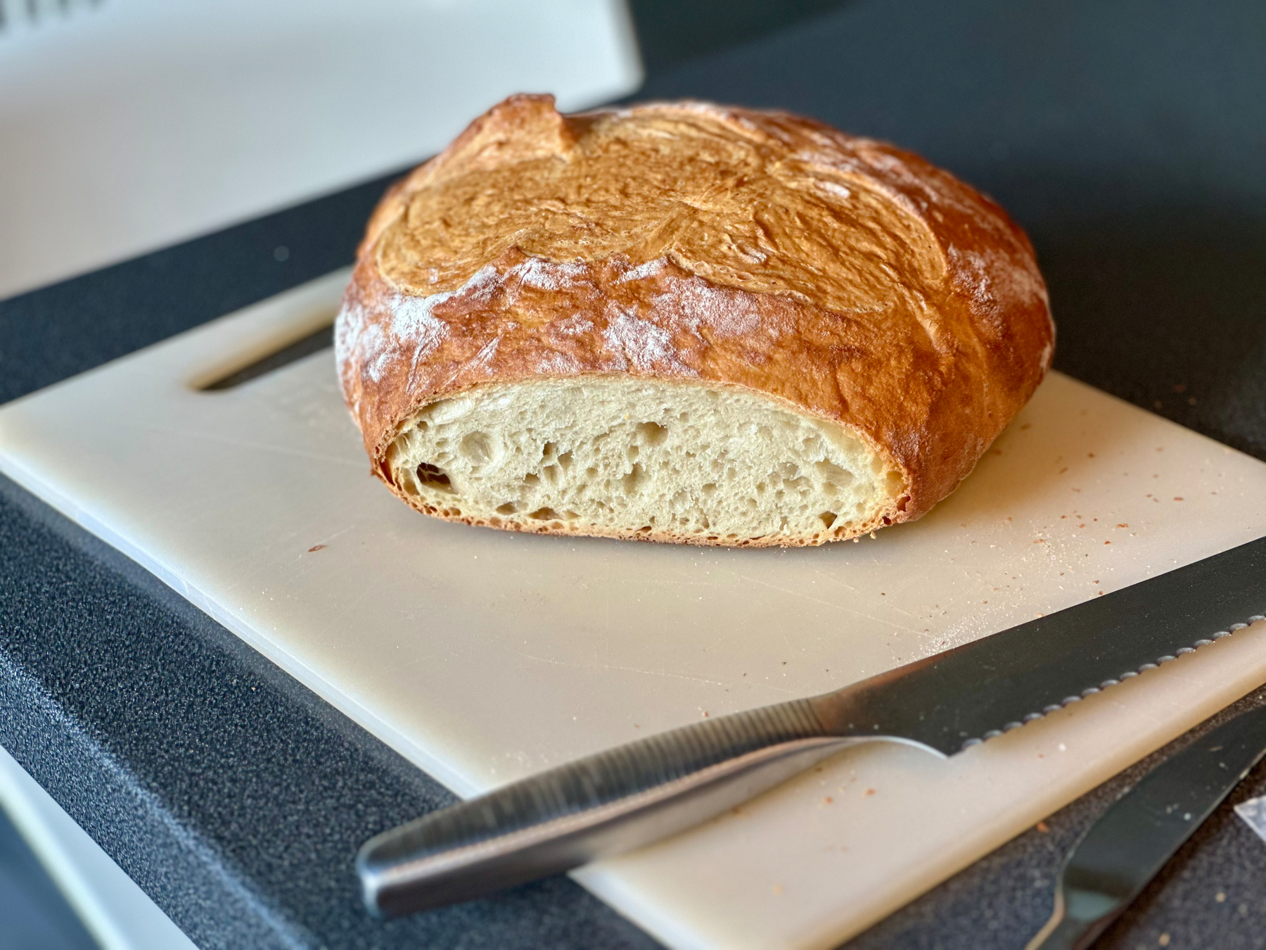 A loaf of crusty bread is sliced in half on a cutting board, next to a serrated knife.