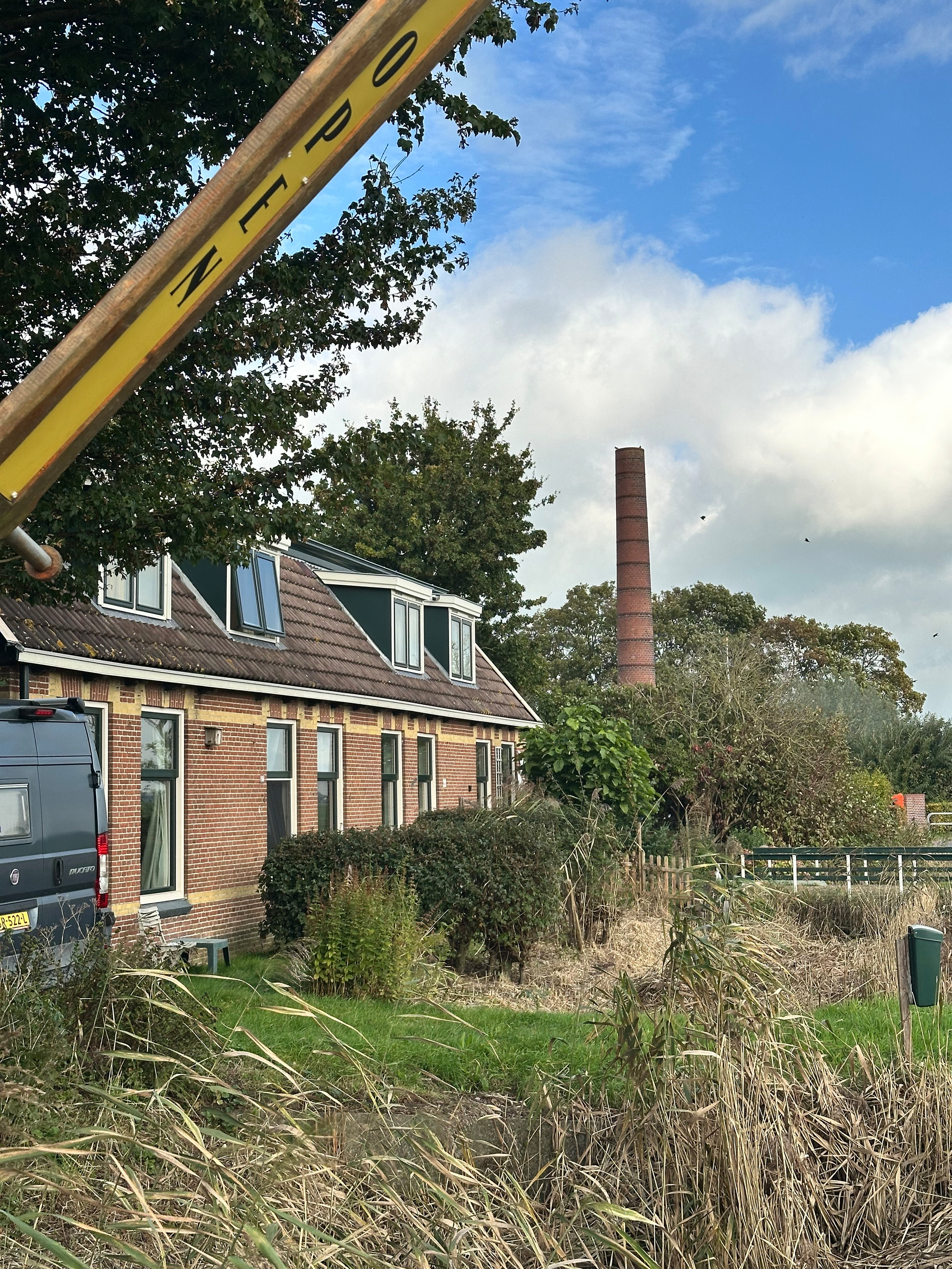 A rural scene features a brick house with dormer windows, a van parked nearby, an old industrial chimney in the background, and a barrier arm with the text ZPLO in the foreground.