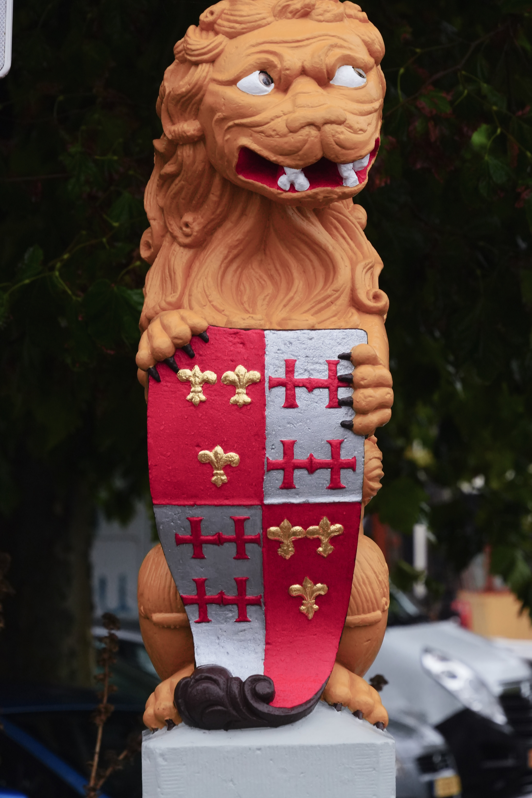 A decorative lion statue is holding a shield adorned with red, silver, and gold heraldic symbols.