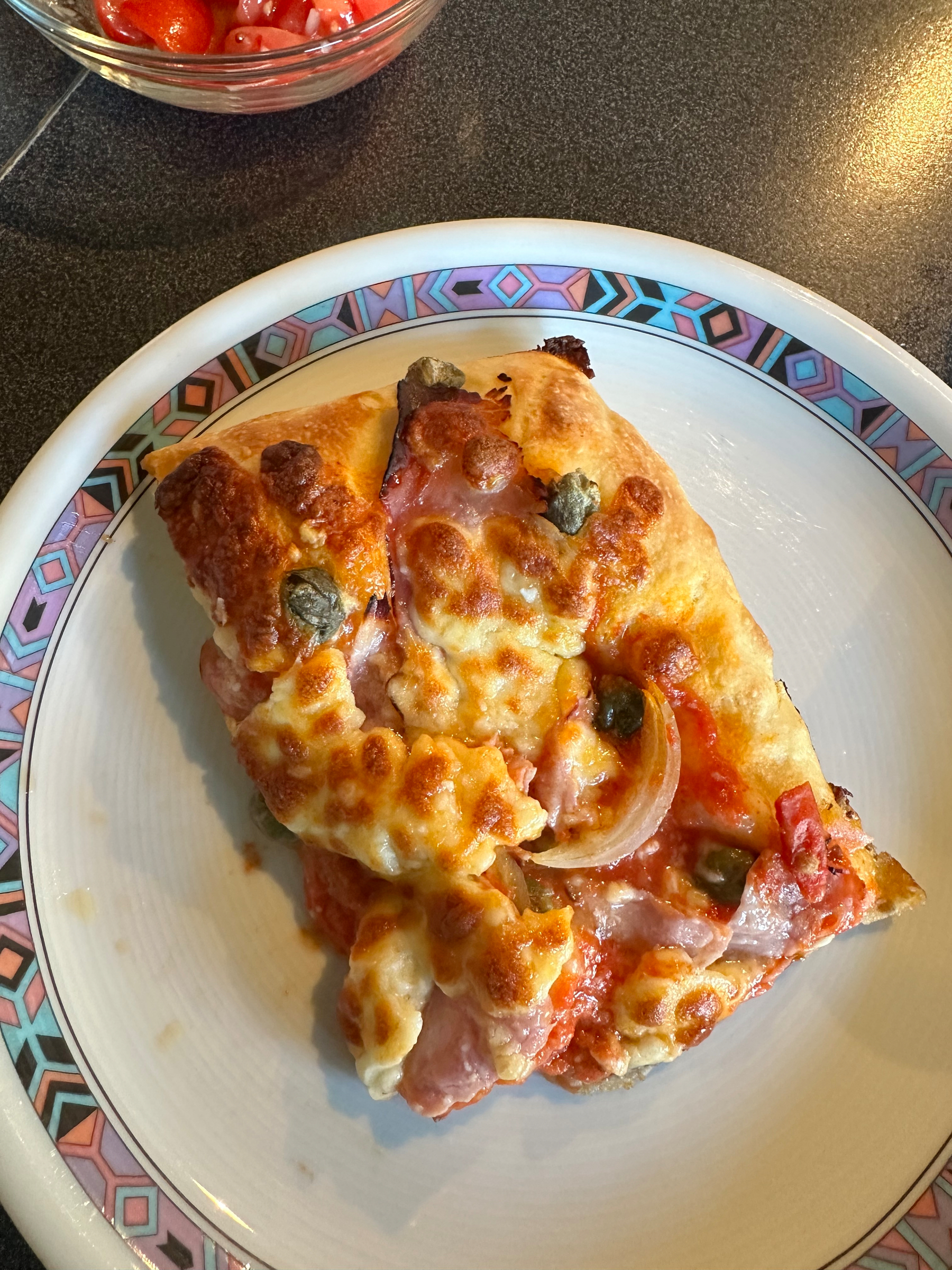 Two slices of pizza topped with melted cheese, ham, onions, and capers are served on a decorative plate.