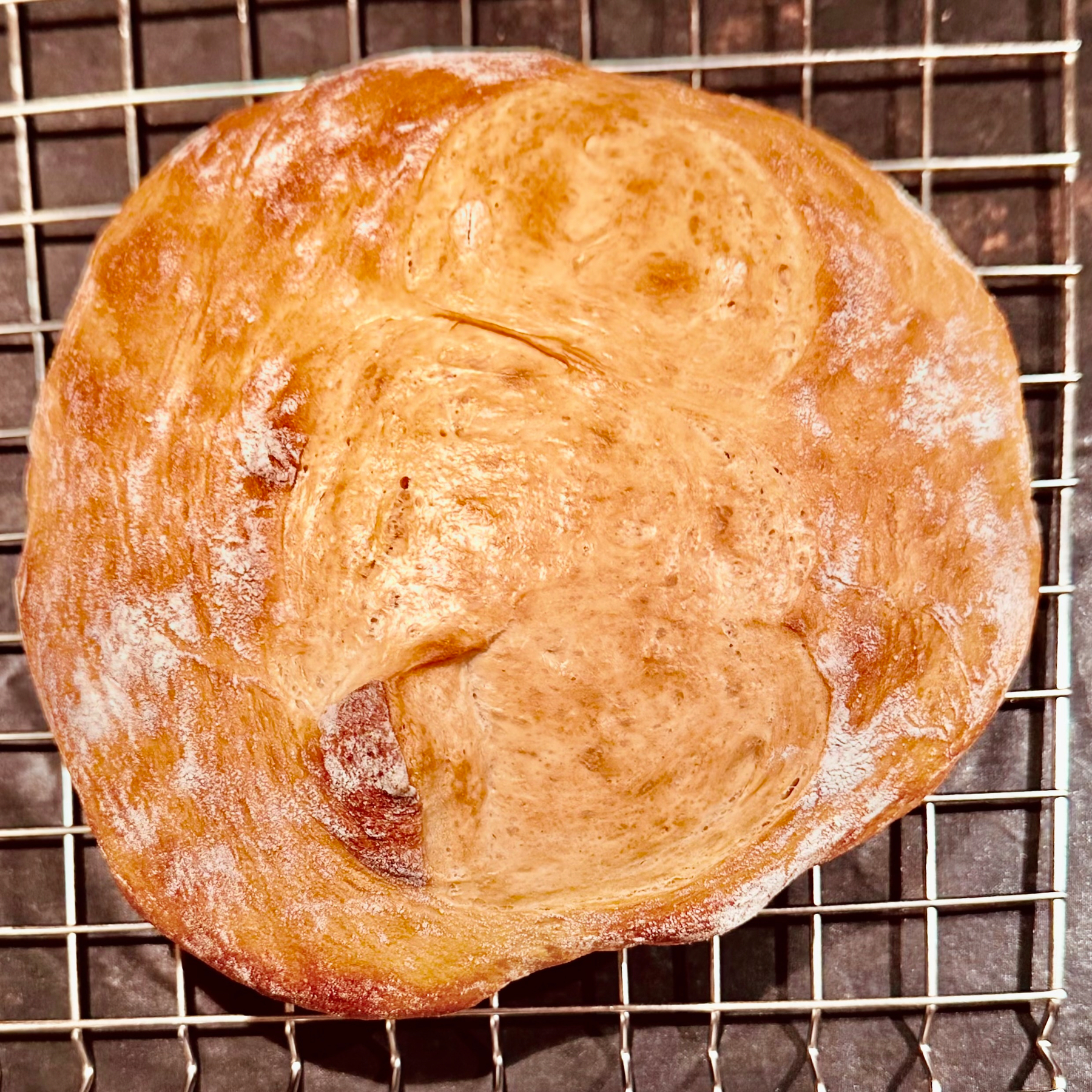 A round loaf of bread with a golden crust rests on a cooling rack.