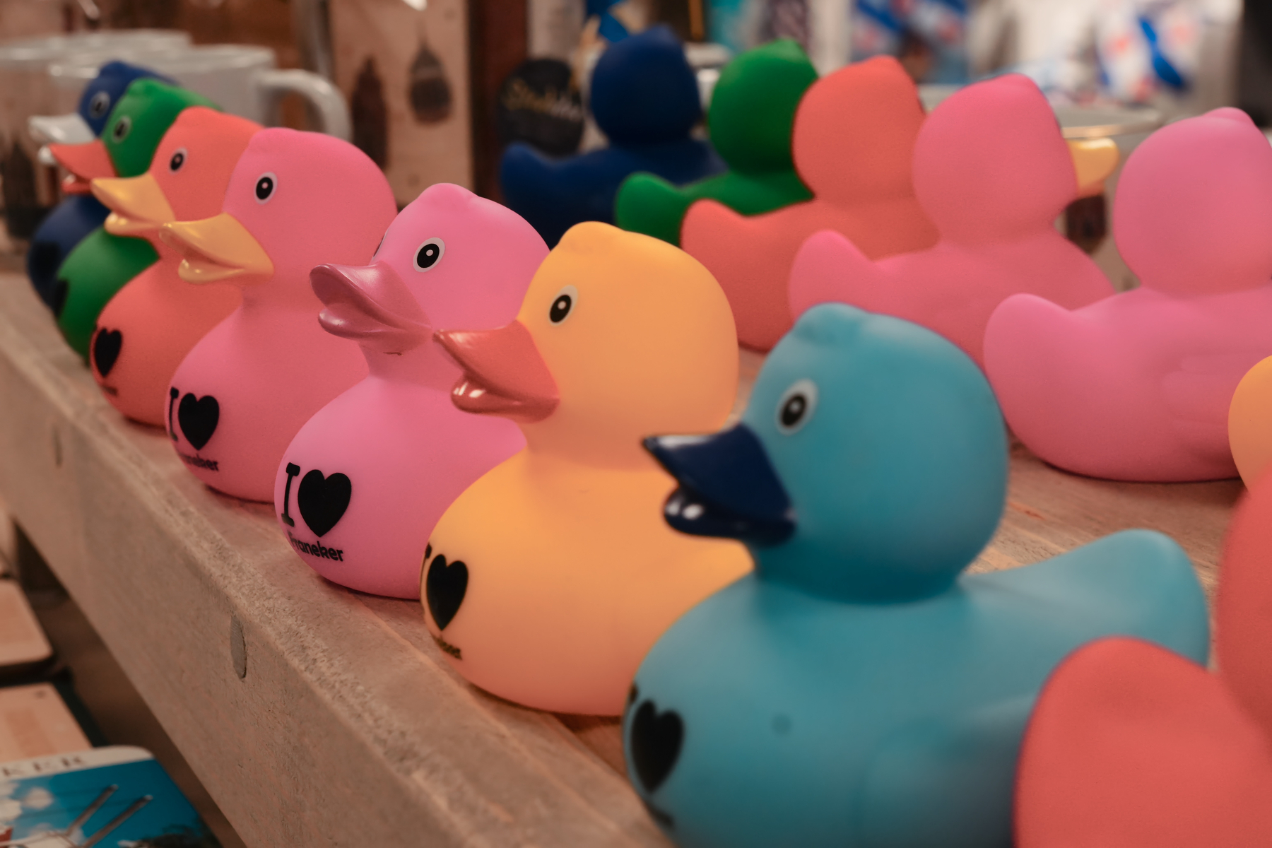 A row of colorful rubber ducks with heart designs is displayed on a wooden shelf.