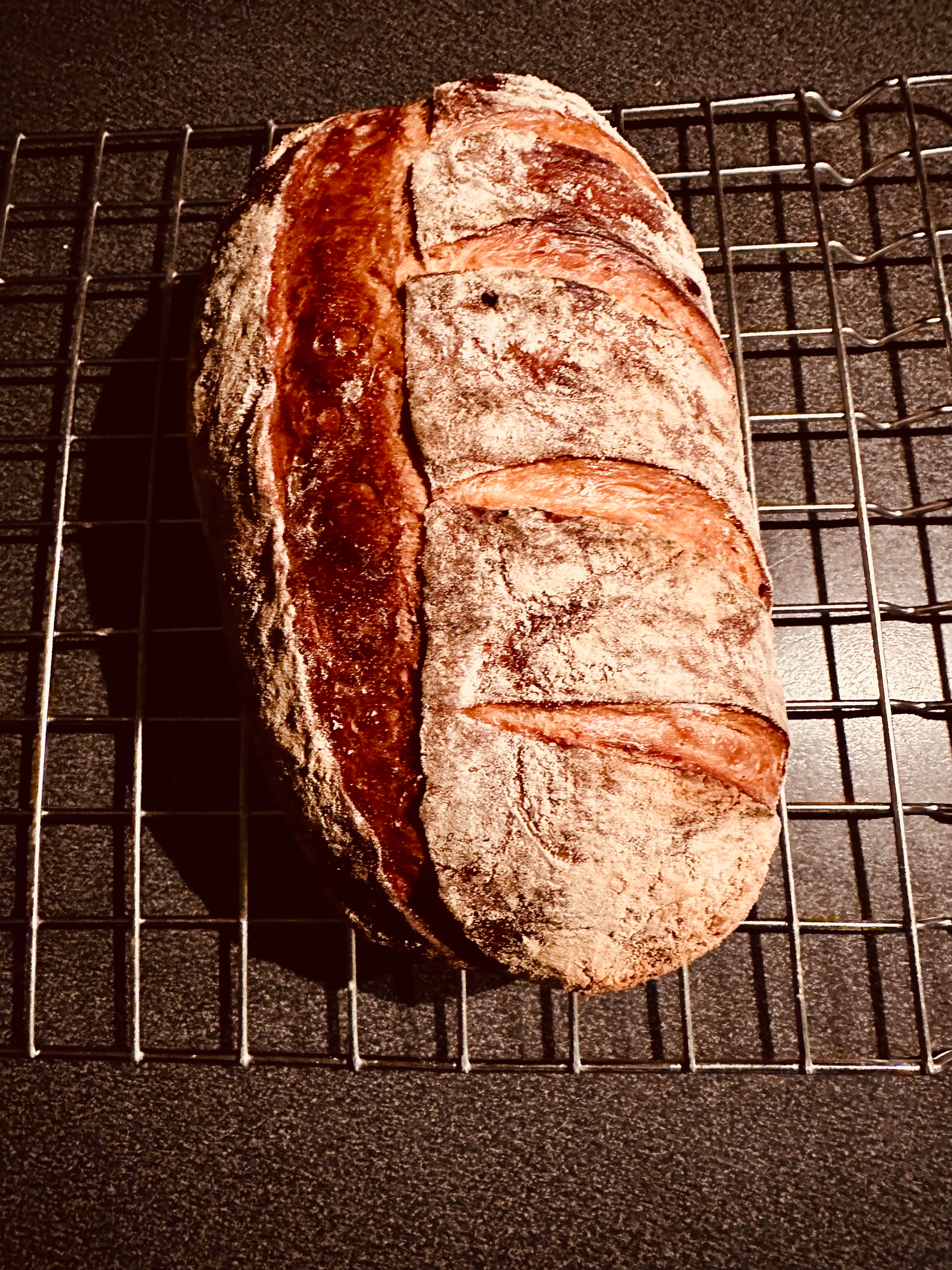A freshly baked dark loaf of bread is cooling on a wire rack.