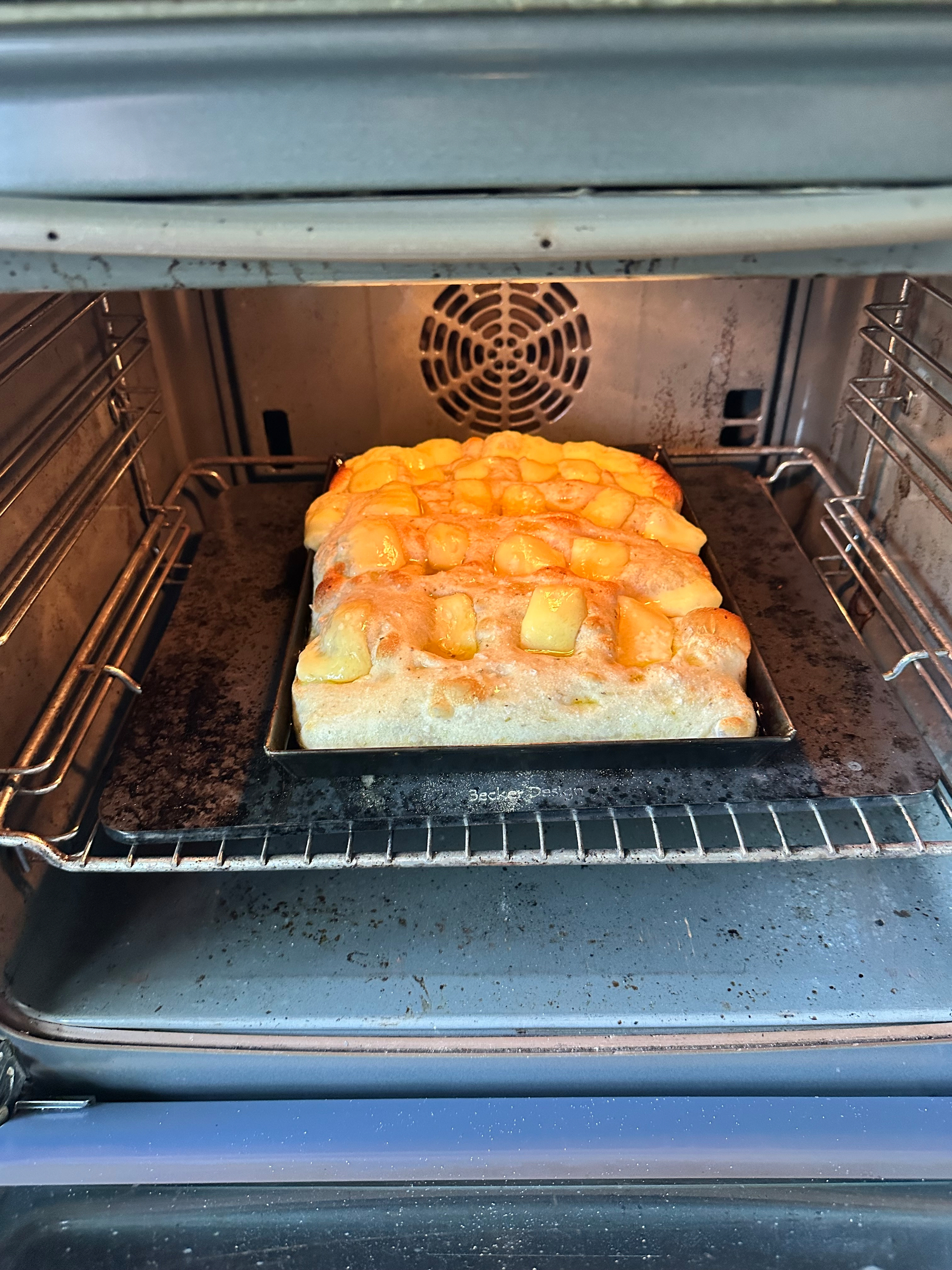 A cheese-topped focaccia is baking inside a metal oven on a tray.