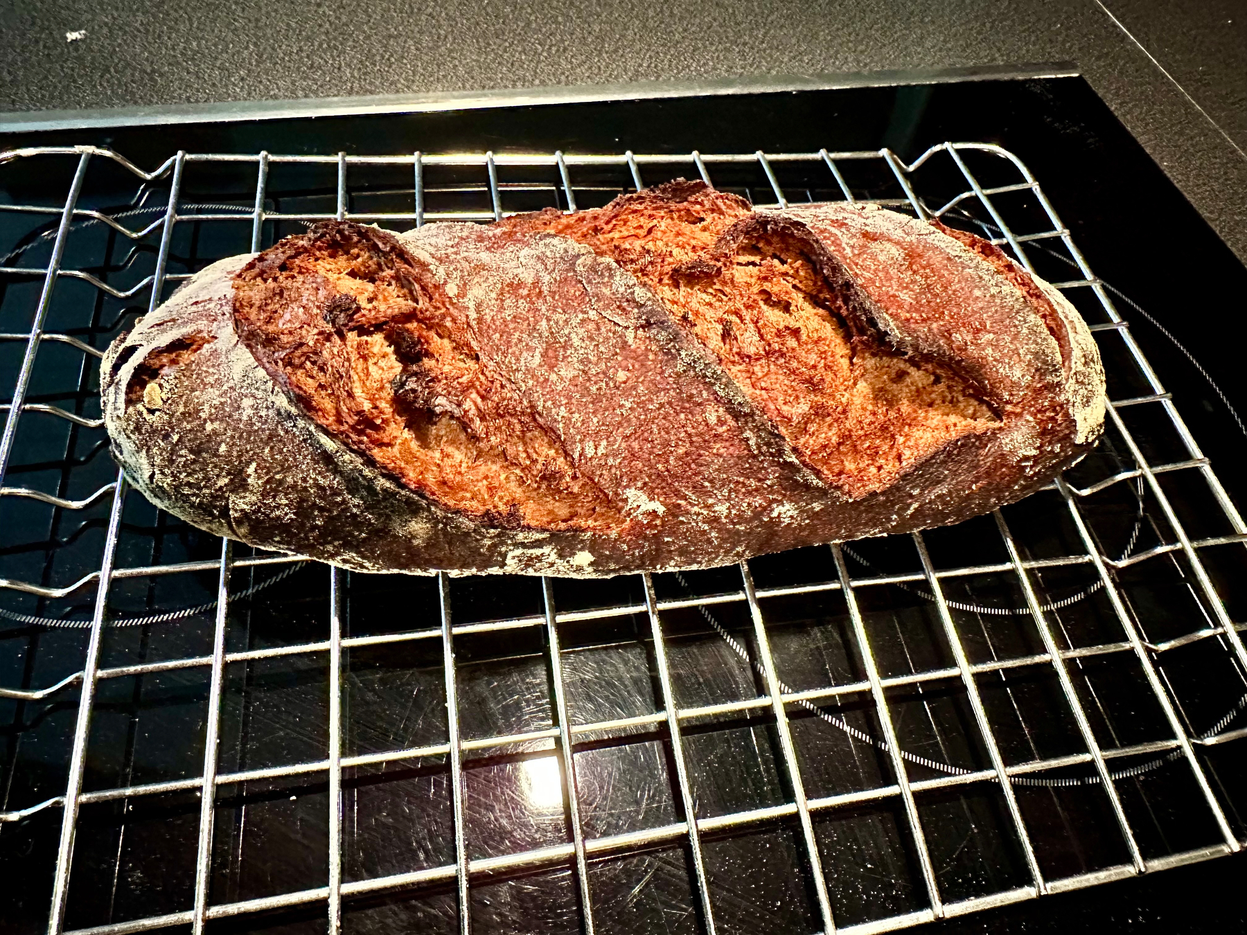 A freshly baked loaf of bread with a crusty, golden-brown exterior rests on a cooling rack.