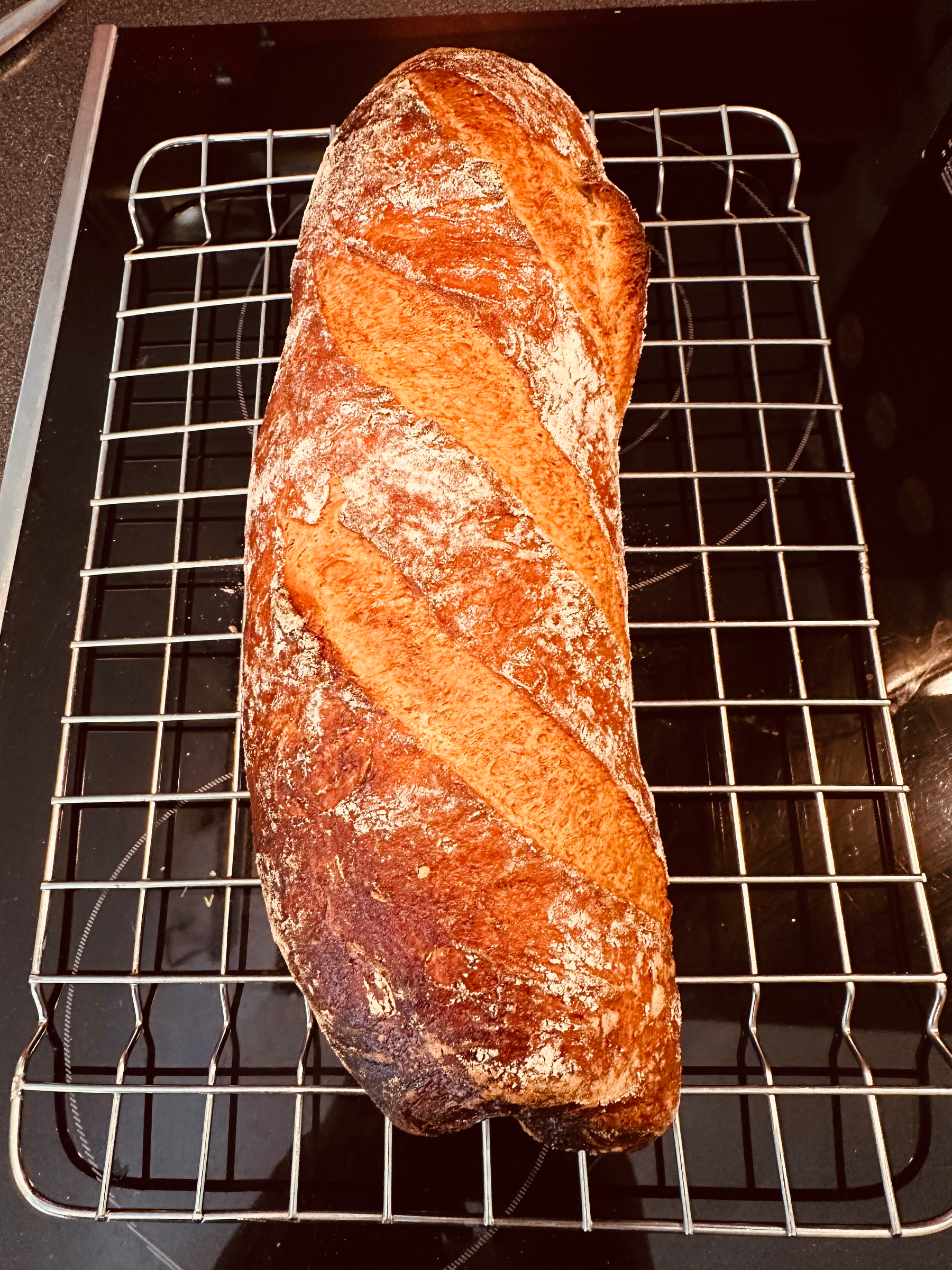 A freshly baked loaf of bread with a golden crust rests on a cooling rack.