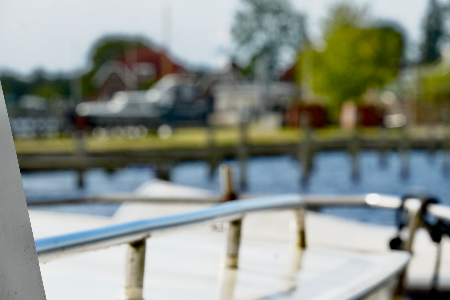 A boat railing and part of a deck are in sharp focus in the foreground with a blurred background of water, a dock, and buildings.
