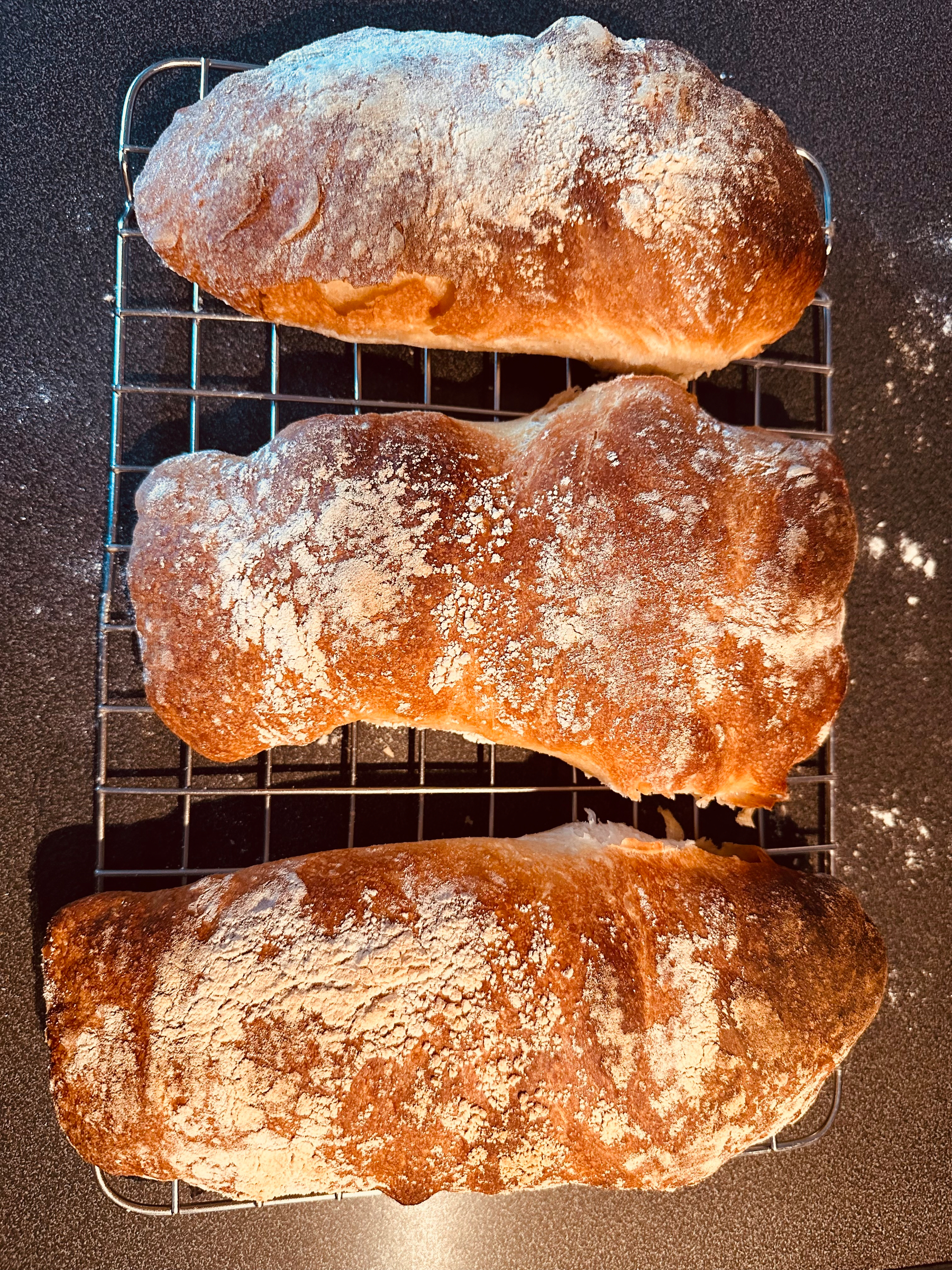 Three freshly baked loaves of ciabatta are cooling on a wire rack.