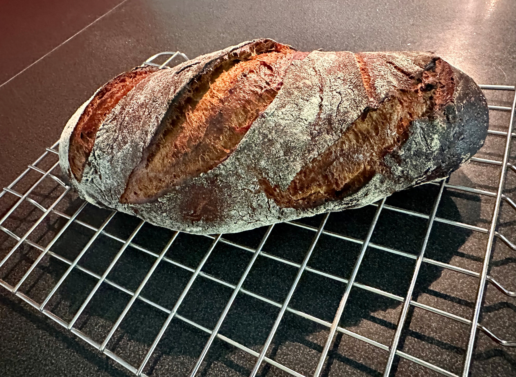 A freshly baked loaf of artisanal bread rests on a wire cooling rack, showcasing its crusty, scored surface.
