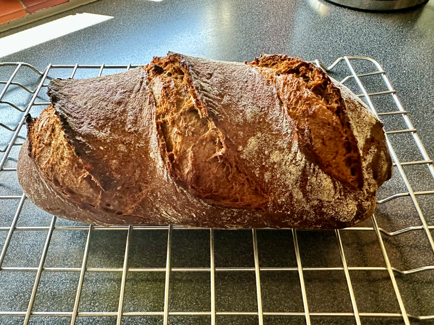 A loaf of crusty, artisanal bread rests on a cooling rack.