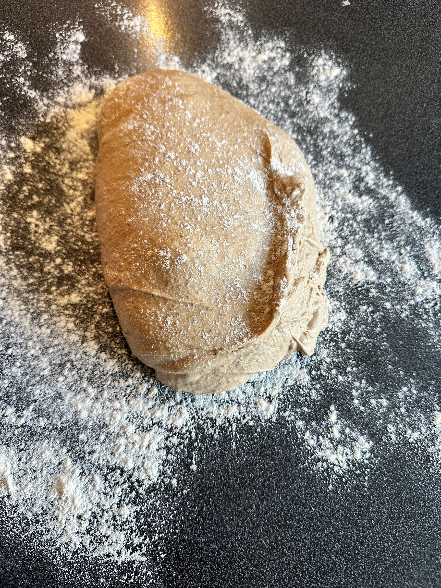 A ball of dough dusted with flour rests on a floured bakers linnen.