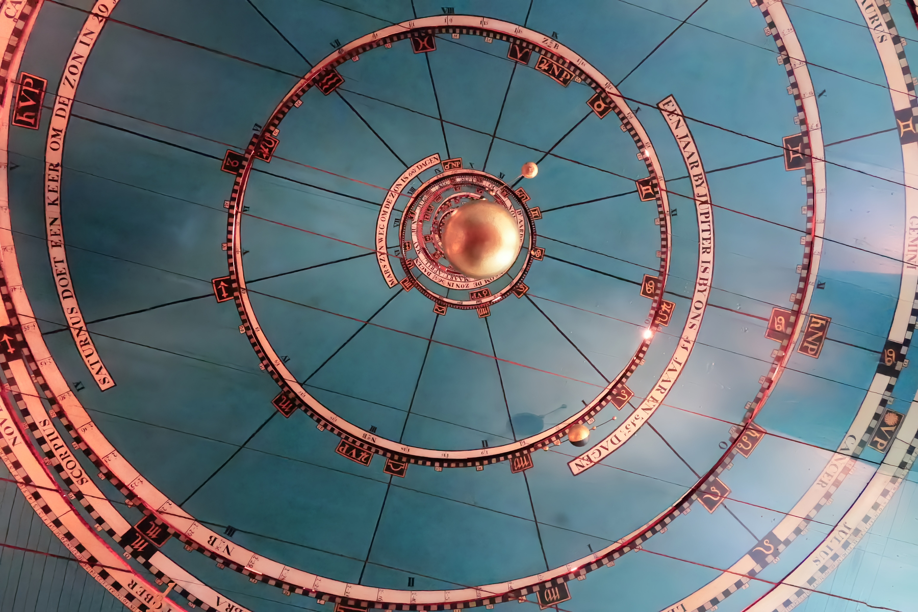 A detailed astronomical ceiling mural depicts a spiral representation of the zodiac signs and celestial movements with a central metallic sphere.