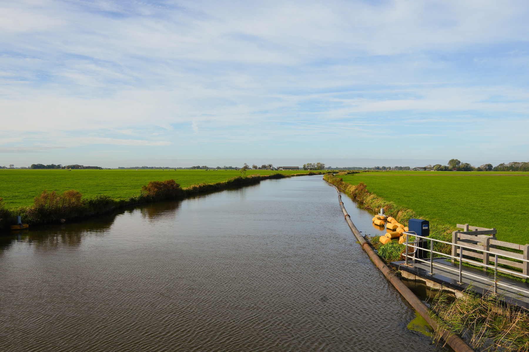 A calm river runs through flat green fields under a partly cloudy sky.