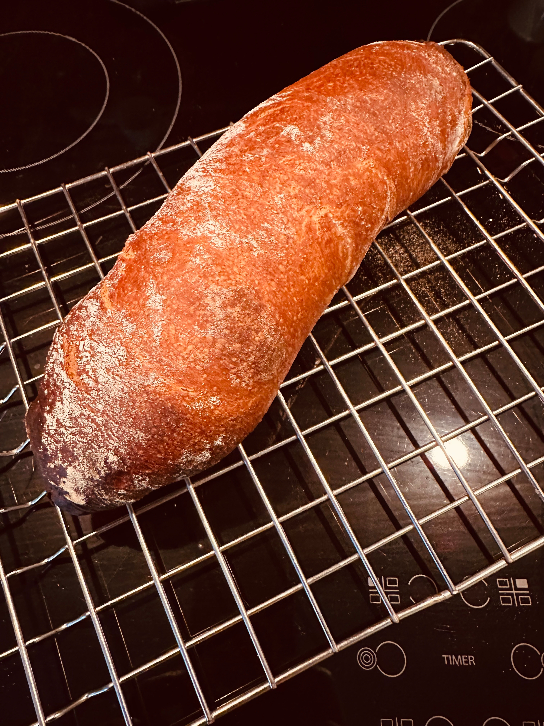A freshly baked loaf of bread cools on a wire rack placed on a stovetop.