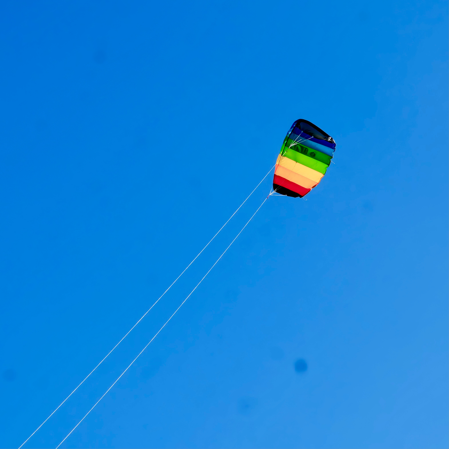 A colorful kite with rainbow stripes is flying high against a clear blue sky.