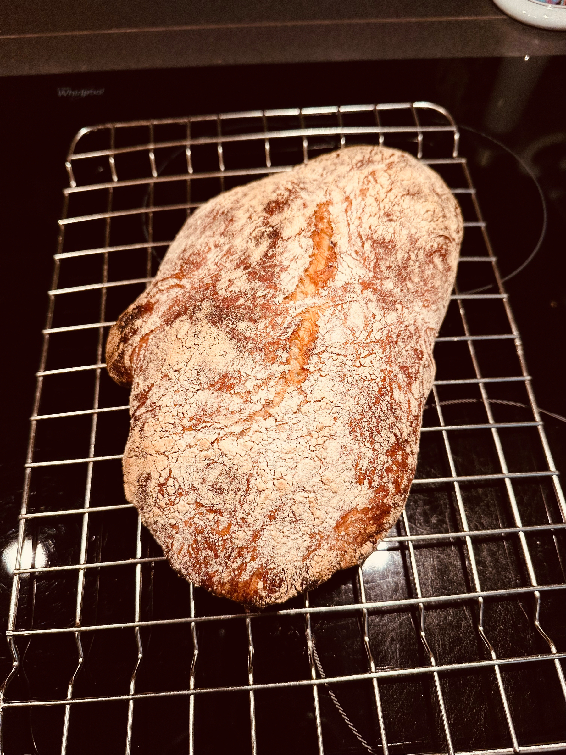 A freshly baked loaf of crusty ciabatta is cooling on a wire rack.