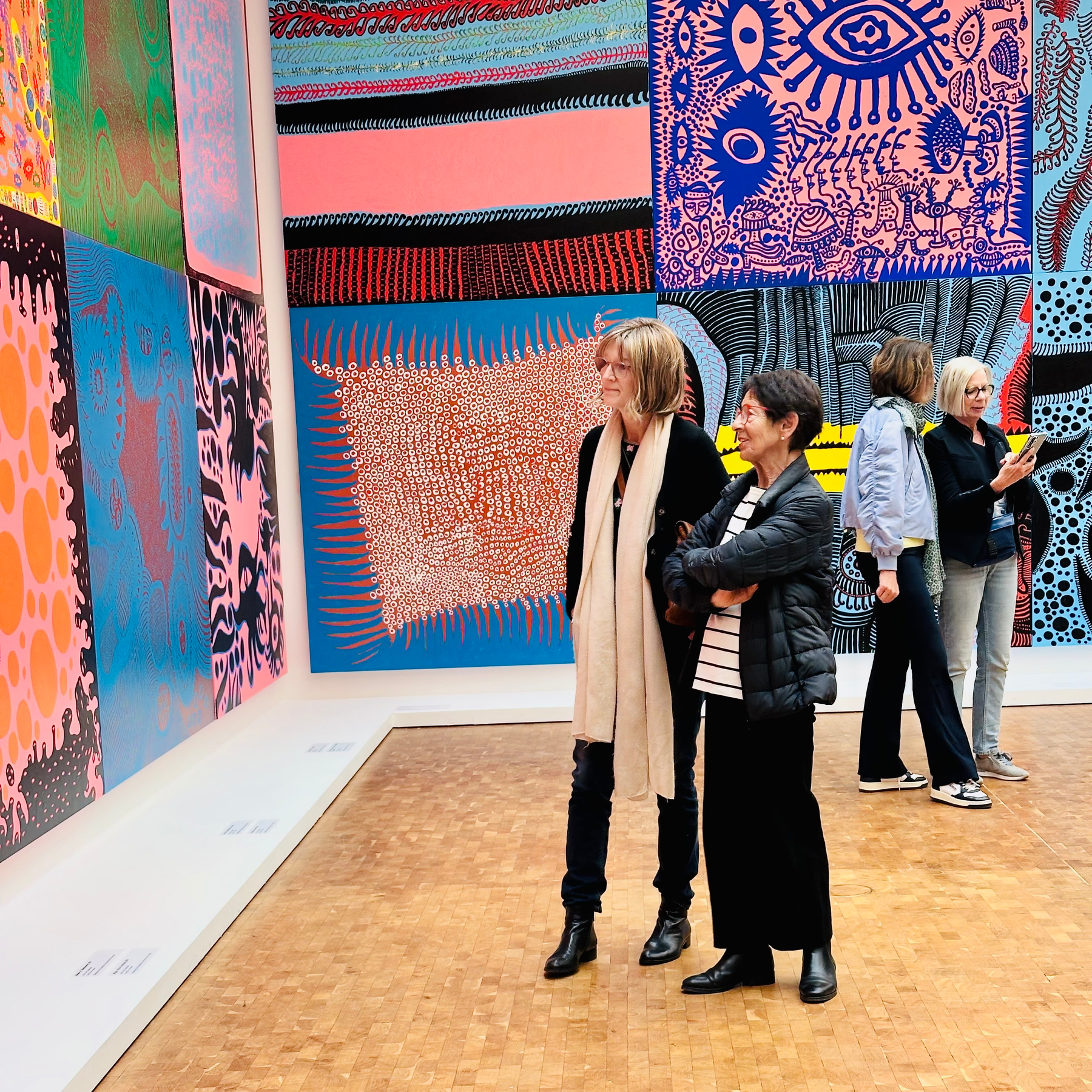 Several people are observing colorful patterned artworks displayed on a gallery wall.