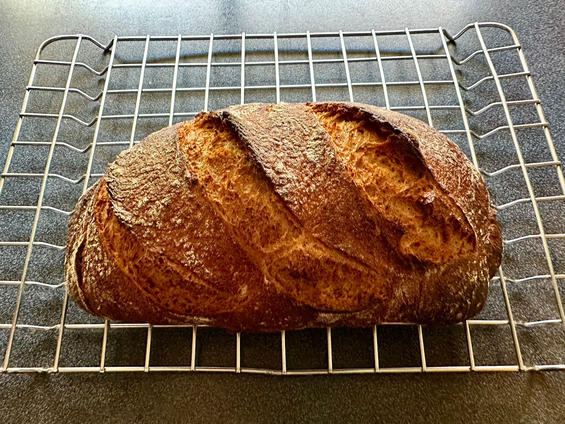 A loaf of crusty bread sits on a cooling rack.